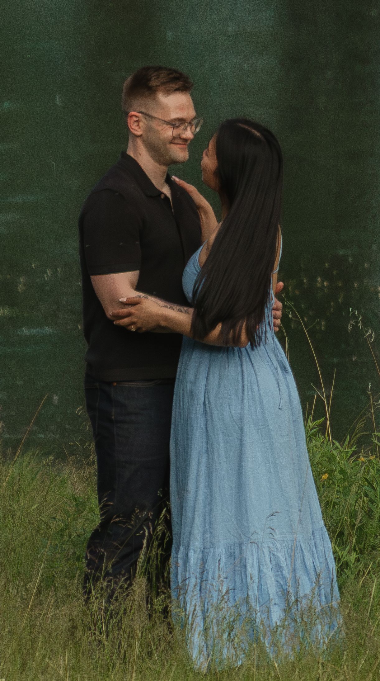 Romantic photoshoot by a lakeside with natural greenery and water reflections in the background.