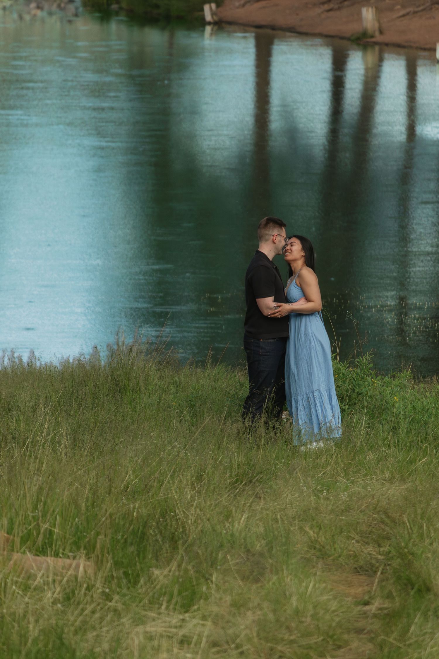 Sweet moment shared between two people near a tranquil lake surrounded by natural grass.