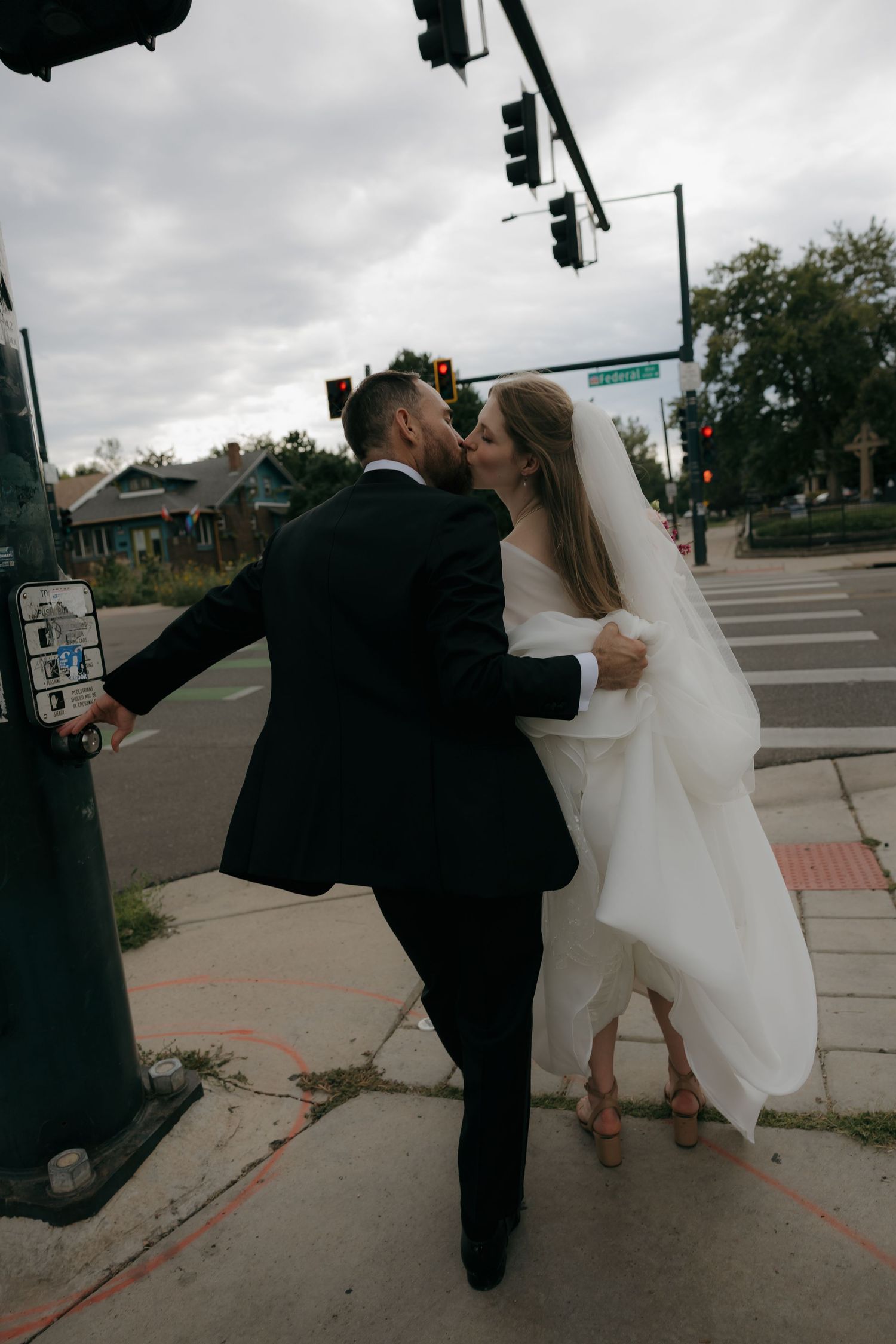 Bride and groom share a kiss at street corner in urban wedding portrait.