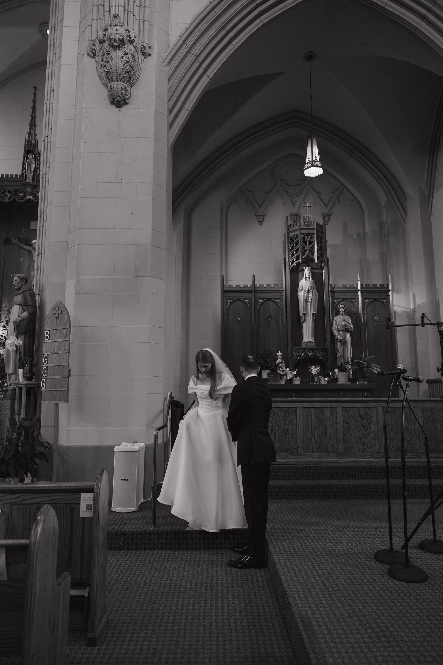 Black and white photo of bride and groom standing together near church altar during wedding ceremony.