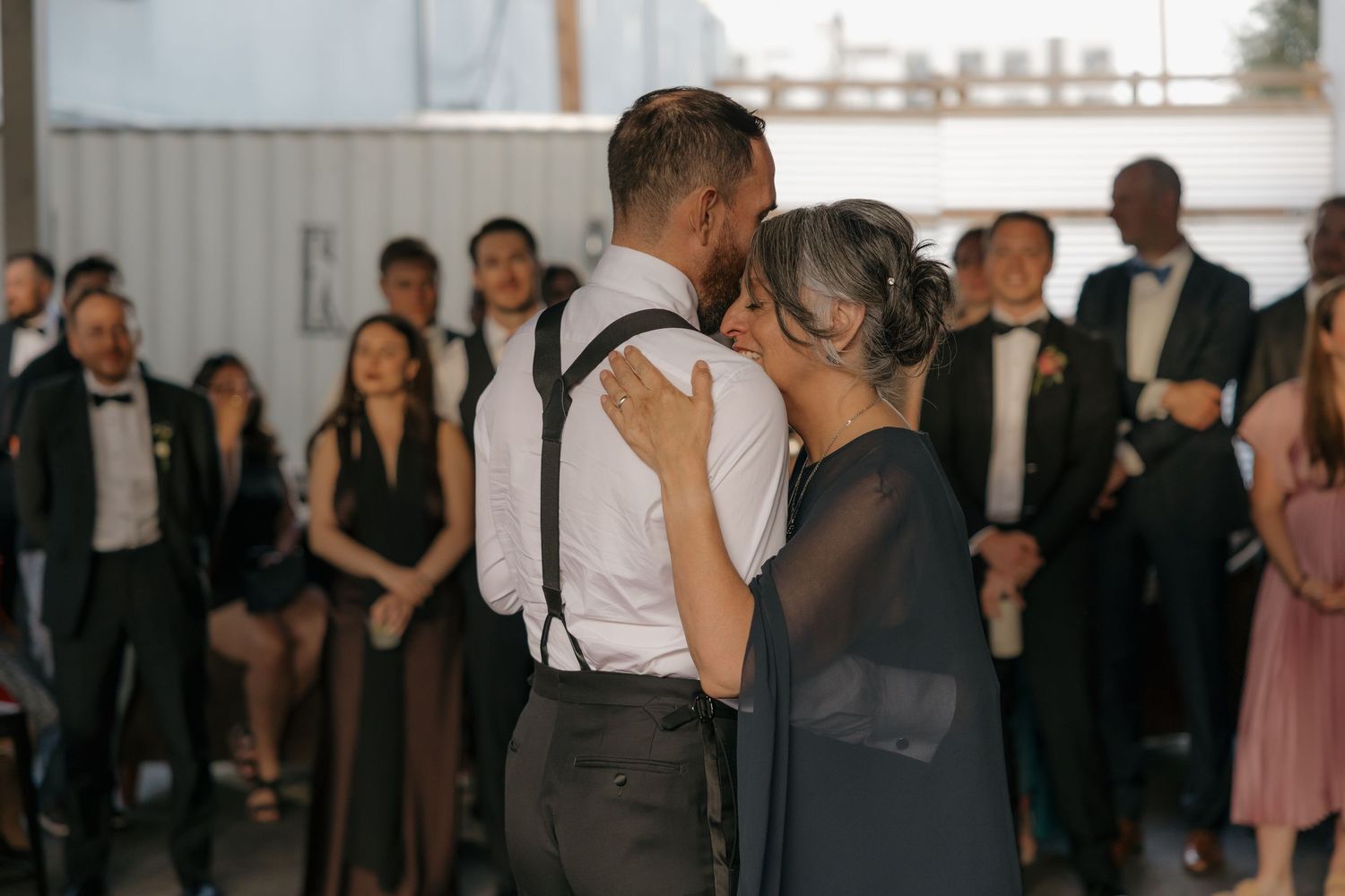 Groom sharing an emotional mother-son dance surrounded by wedding guests at reception.