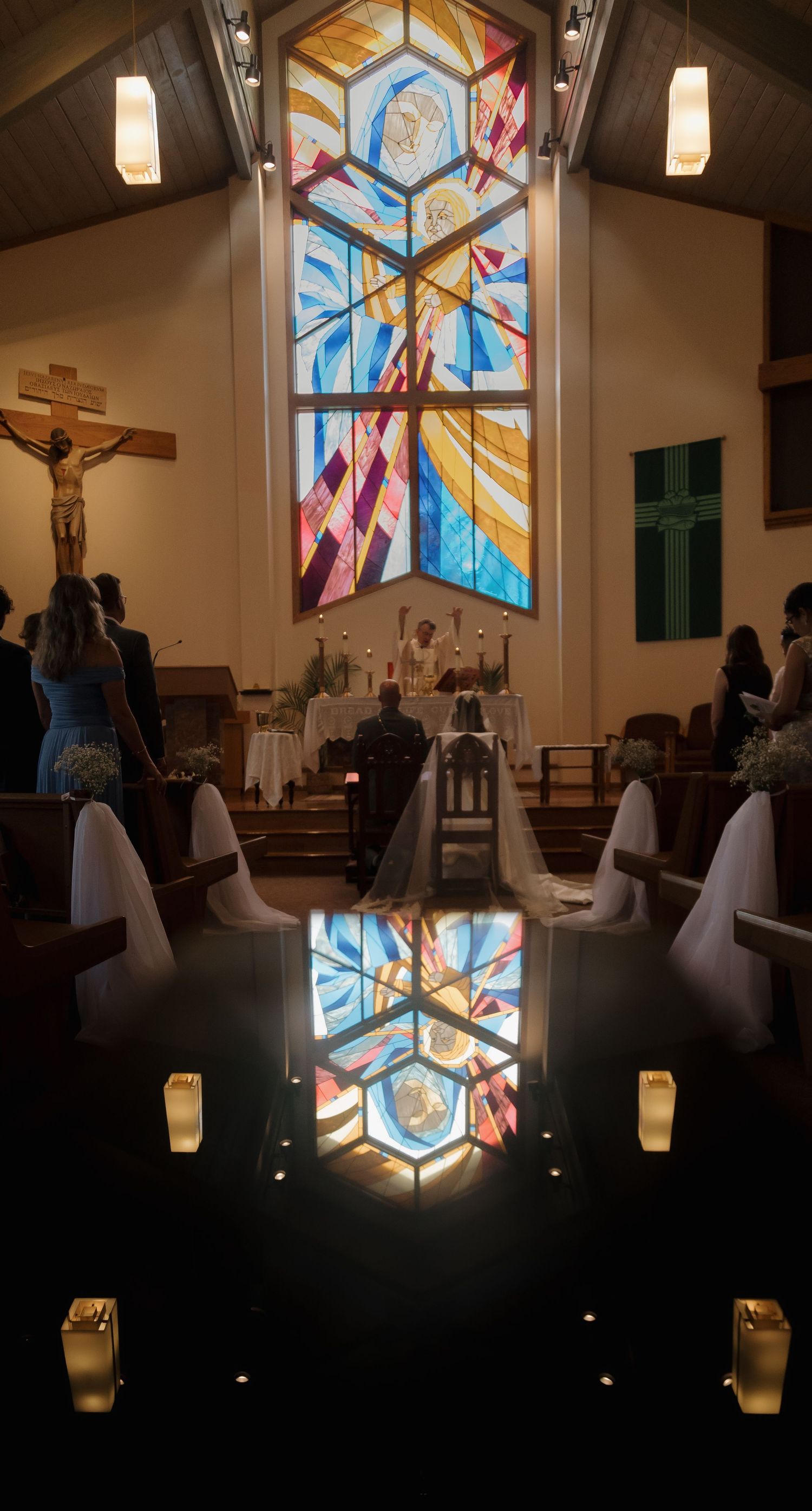 Elegant church wedding aisle with candles reflecting stained glass window and bride at the altar.