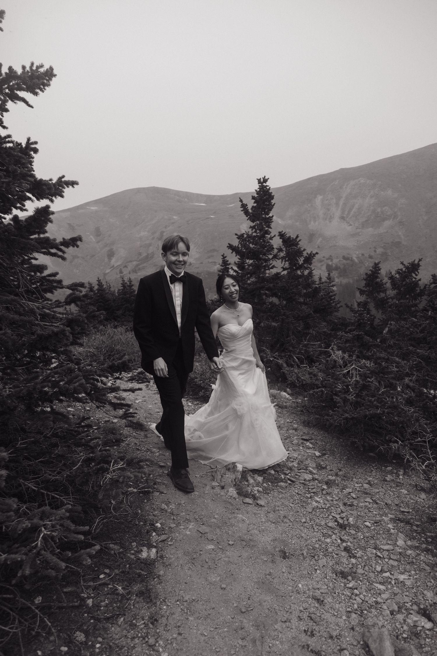 Black and white photo of bride and groom laughing while walking a mountain forest trail during elopement.