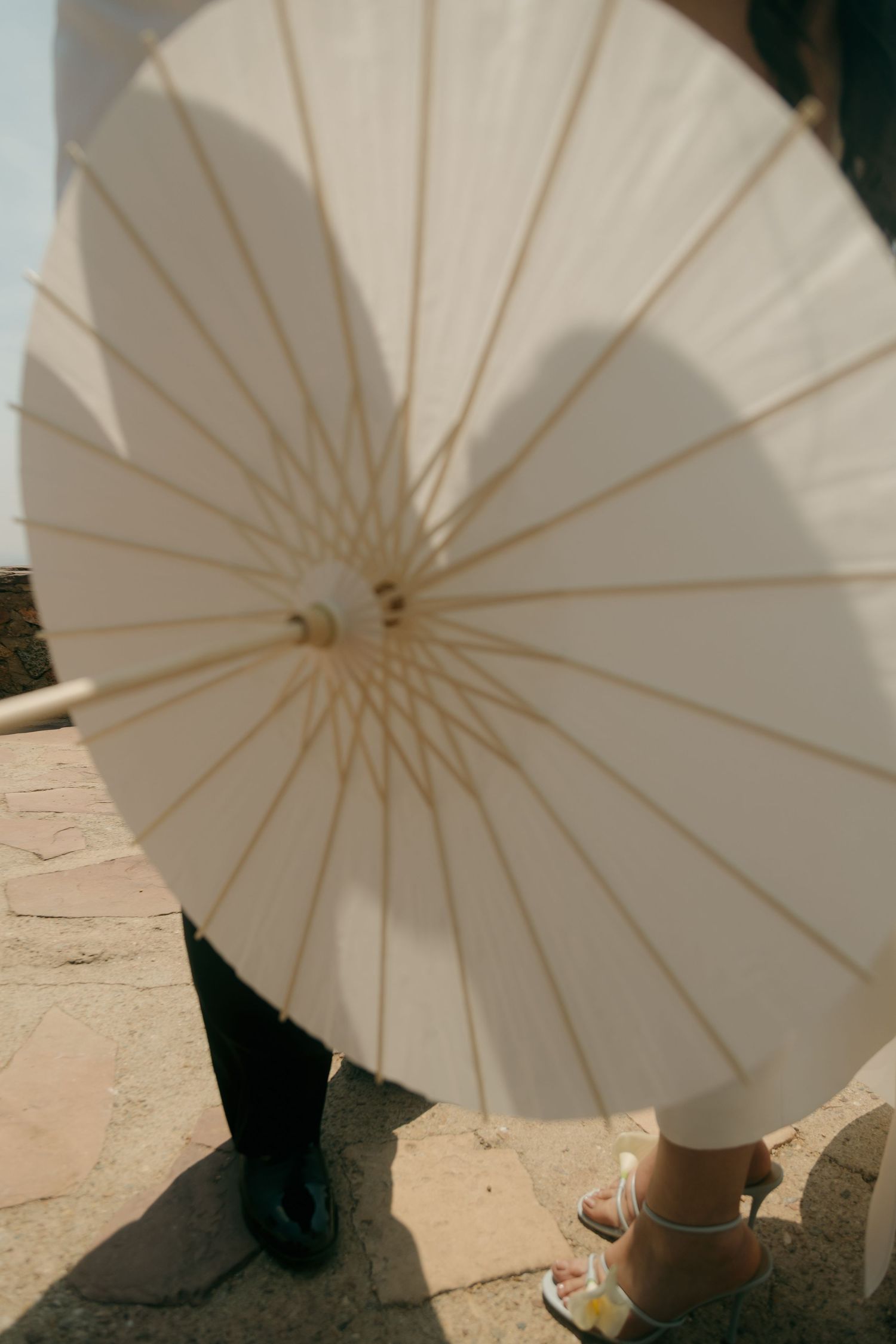 Close-up of white paper parasol with couple's feet visible on stone ground.