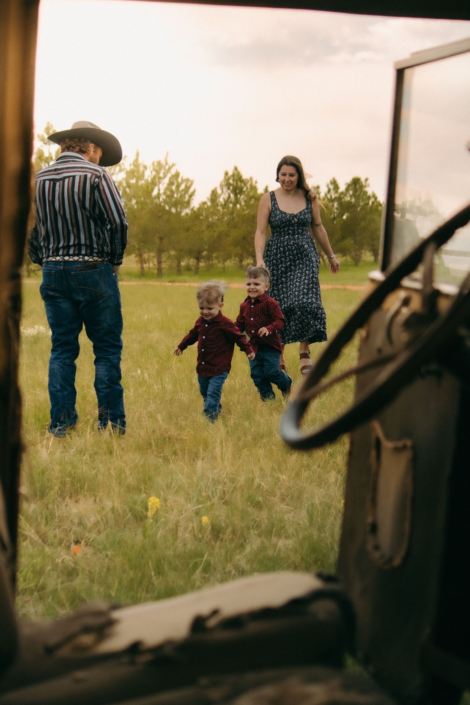 Family playing in a grassy field viewed through the window of an antique truck.