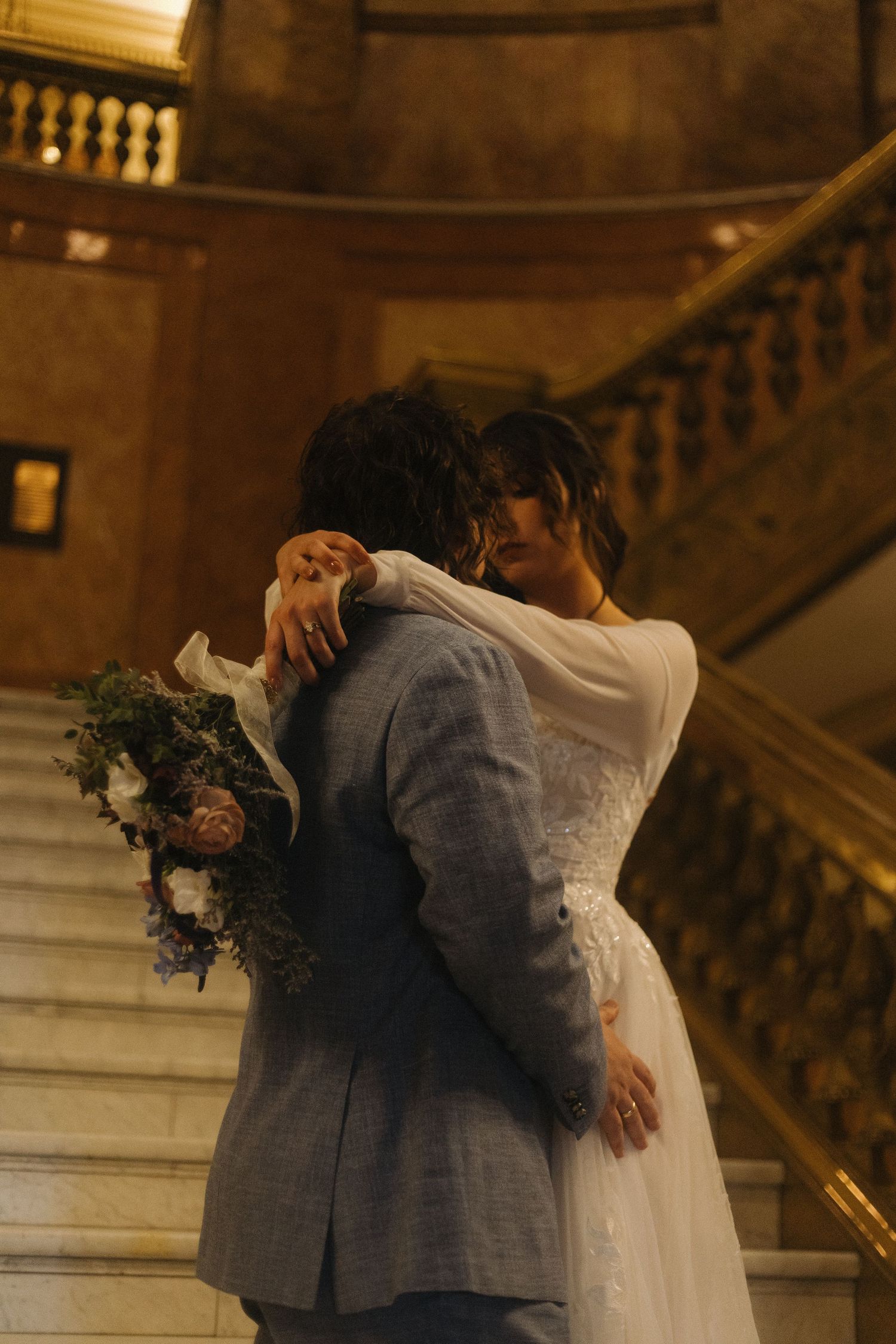 A romantic embrace on an ornate staircase with a wedding bouquet in hand.