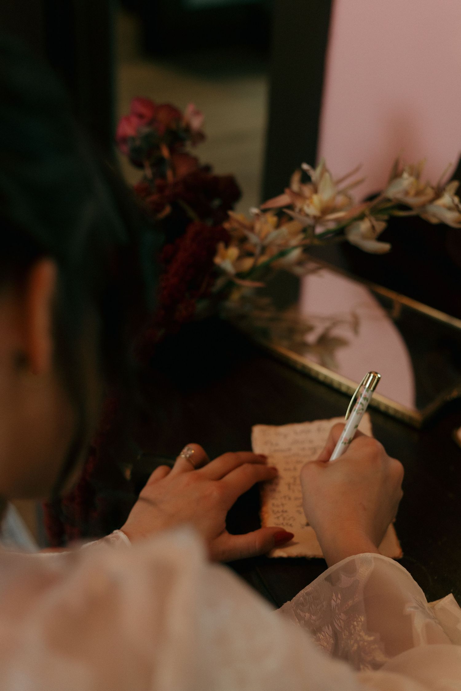 Close-up view of hands writing on paper with delicate pink flowers in soft focus background.