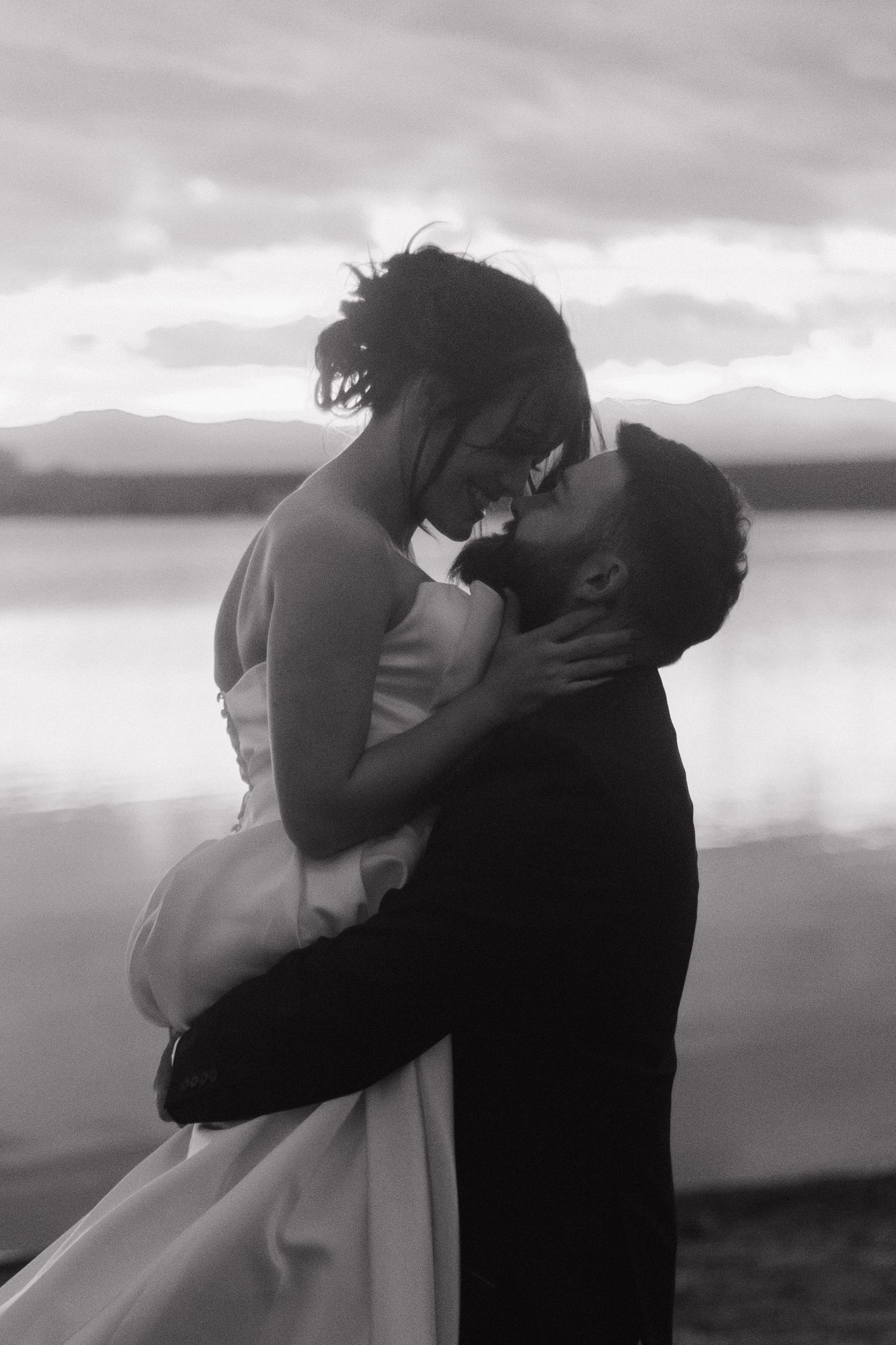 A romantic black and white silhouette of a couple embracing against a waterfront backdrop.