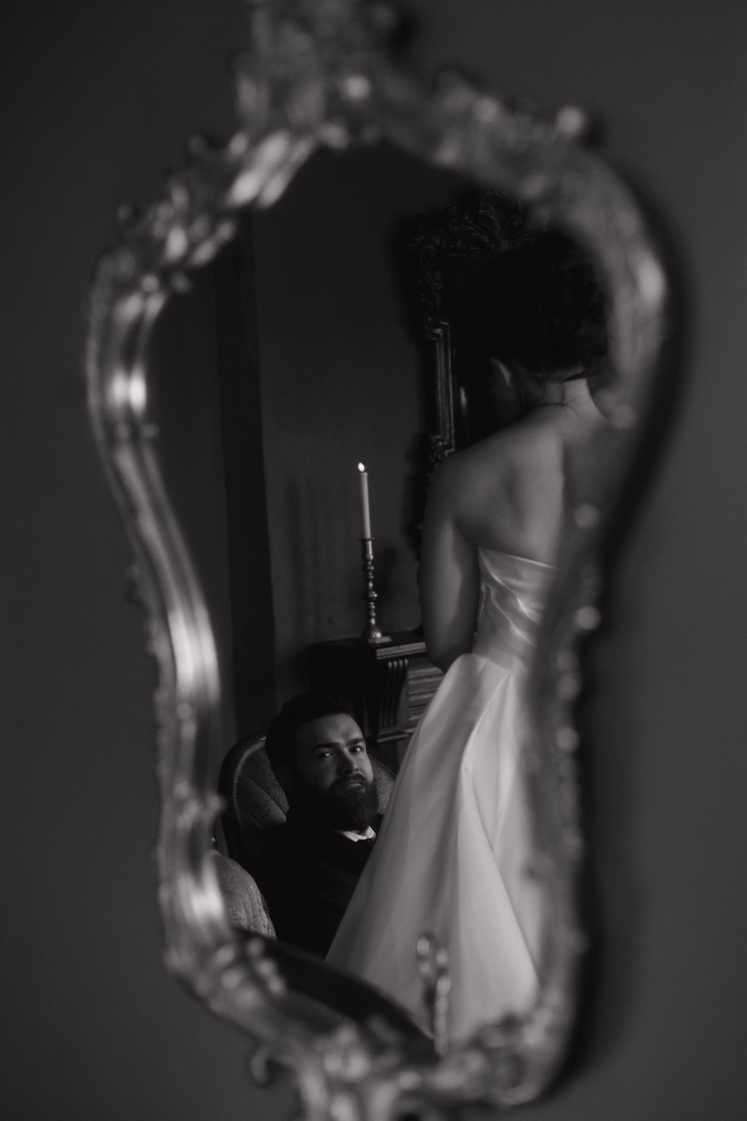 Artistic black and white reflection of a wedding dress in an ornate mirror.