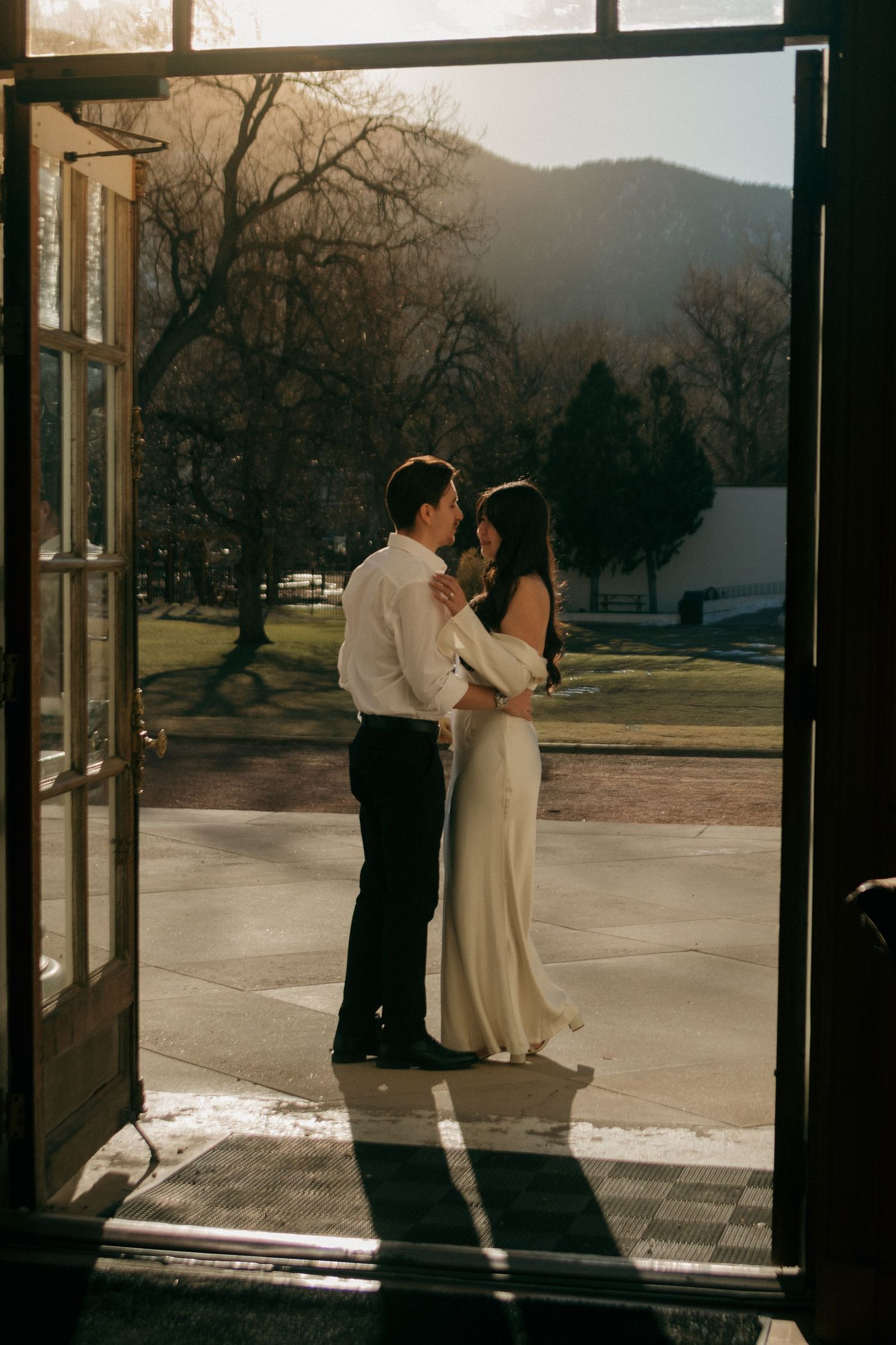 A couple dances together in silhouette against large windows during golden hour.