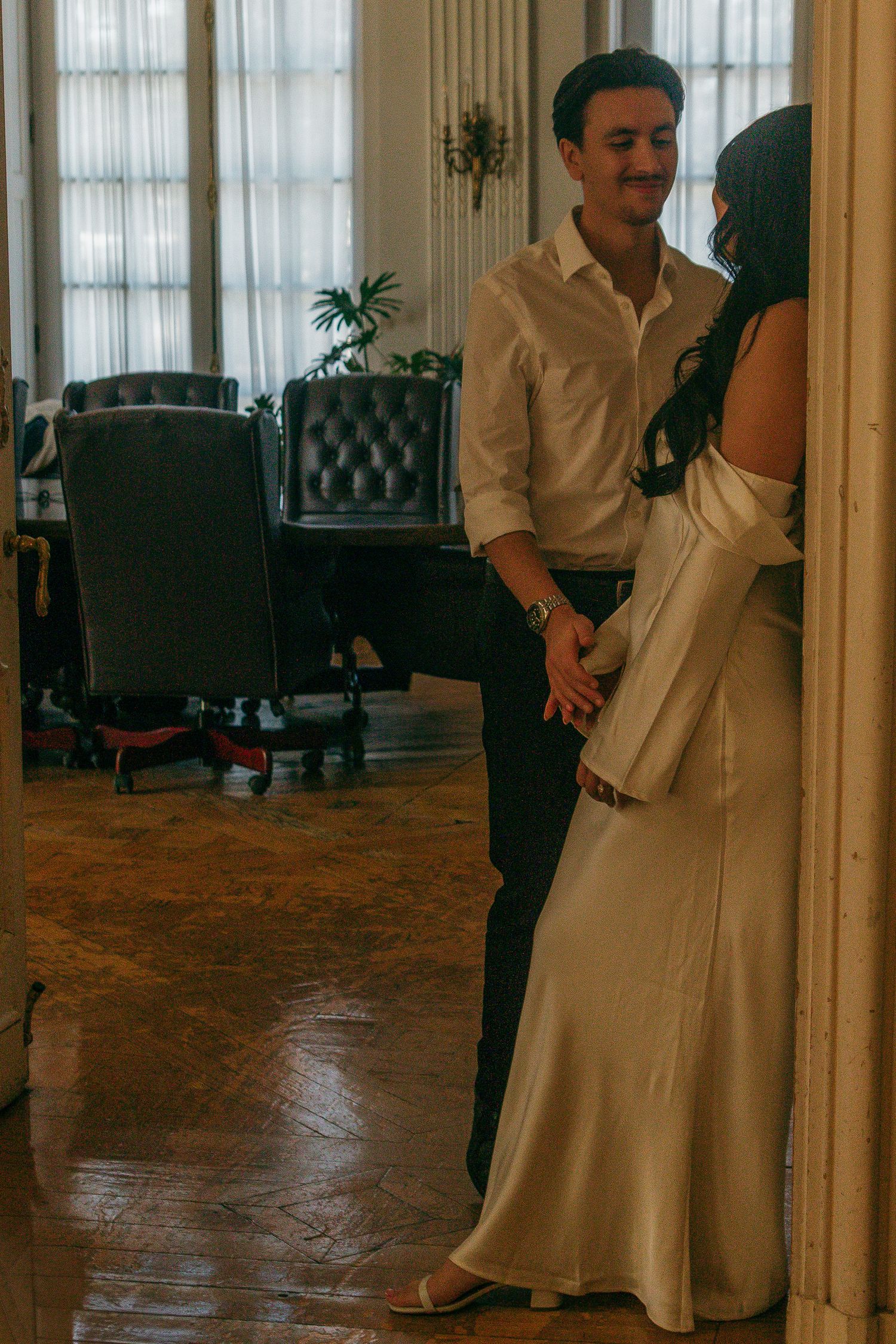 Couple shares romantic moment in elegant room with leather chairs and flowing curtains.
