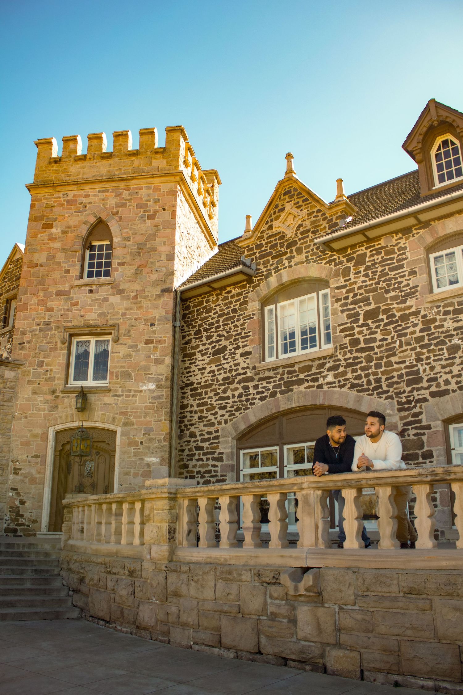 Couple leaning on stone balcony of castle-like building with medieval architecture.