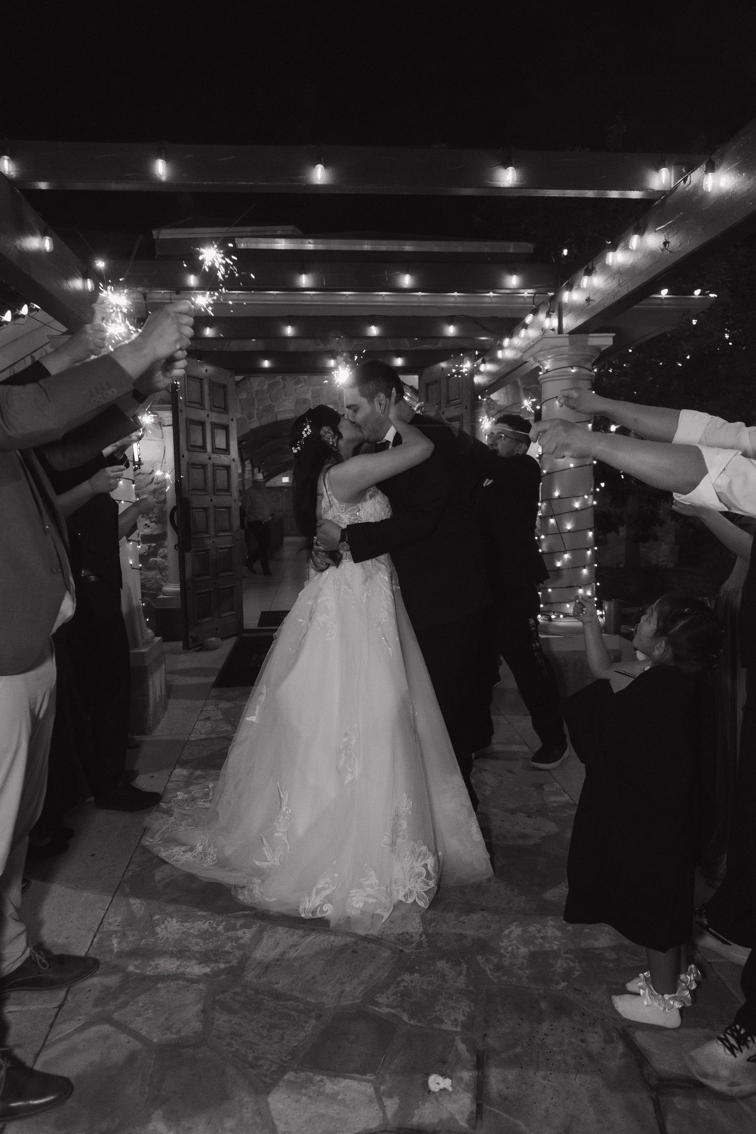 Bride and groom share a kiss during sparkler send-off at night wedding exit.