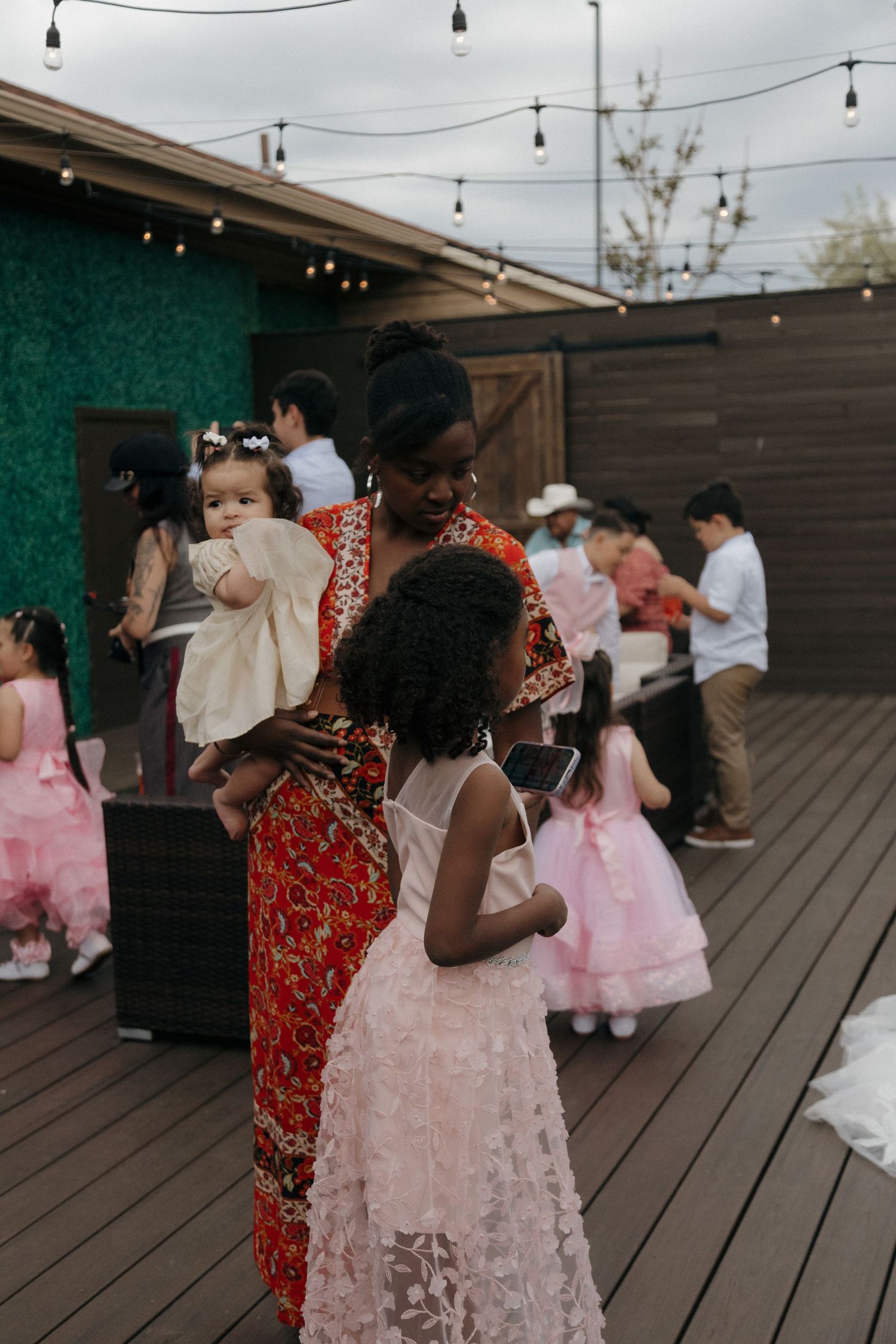 Woman in colorful dress holding baby while interacting with young girl at wedding reception.