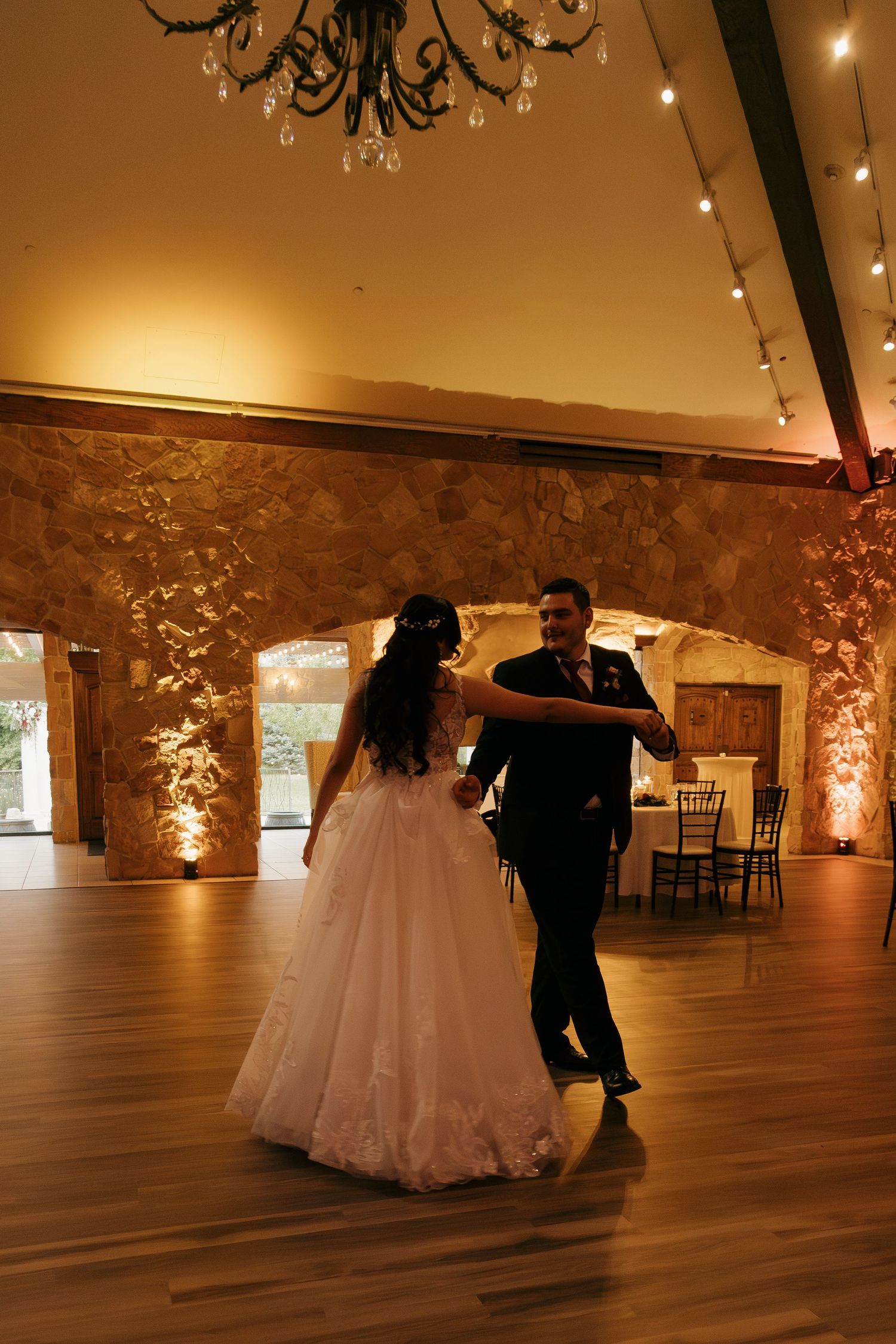 Bride and groom share their first dance under warm lights in a rustic stone ballroom.