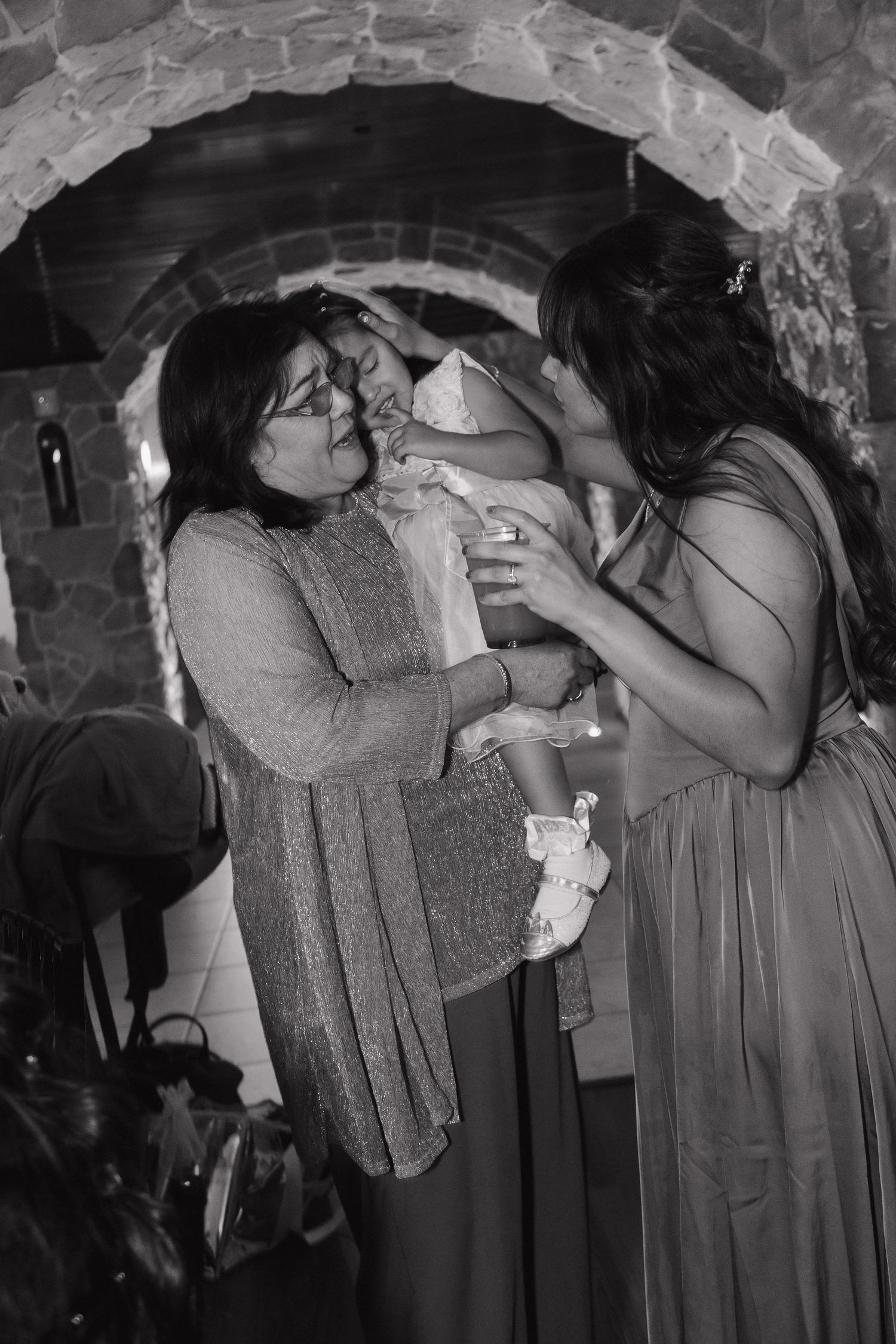 Black and white photo of two women lovingly holding and admiring a baby at a wedding reception.
