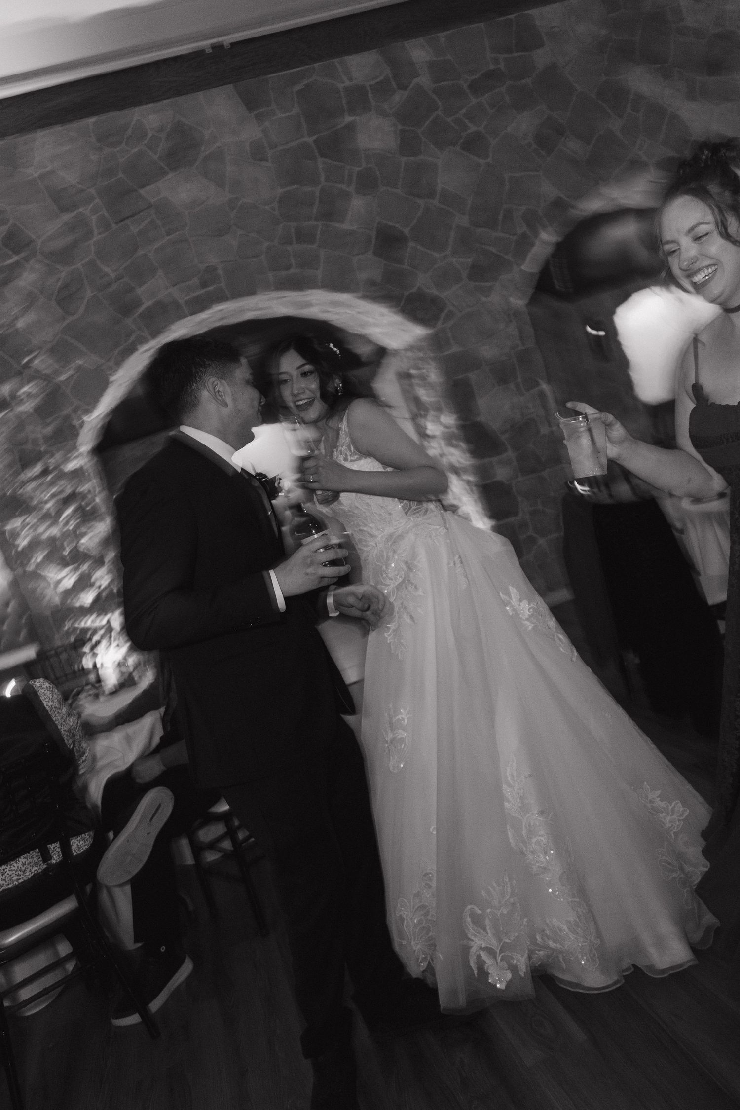 Bride and groom dance joyfully with guests celebrating at lively wedding reception in stone venue.