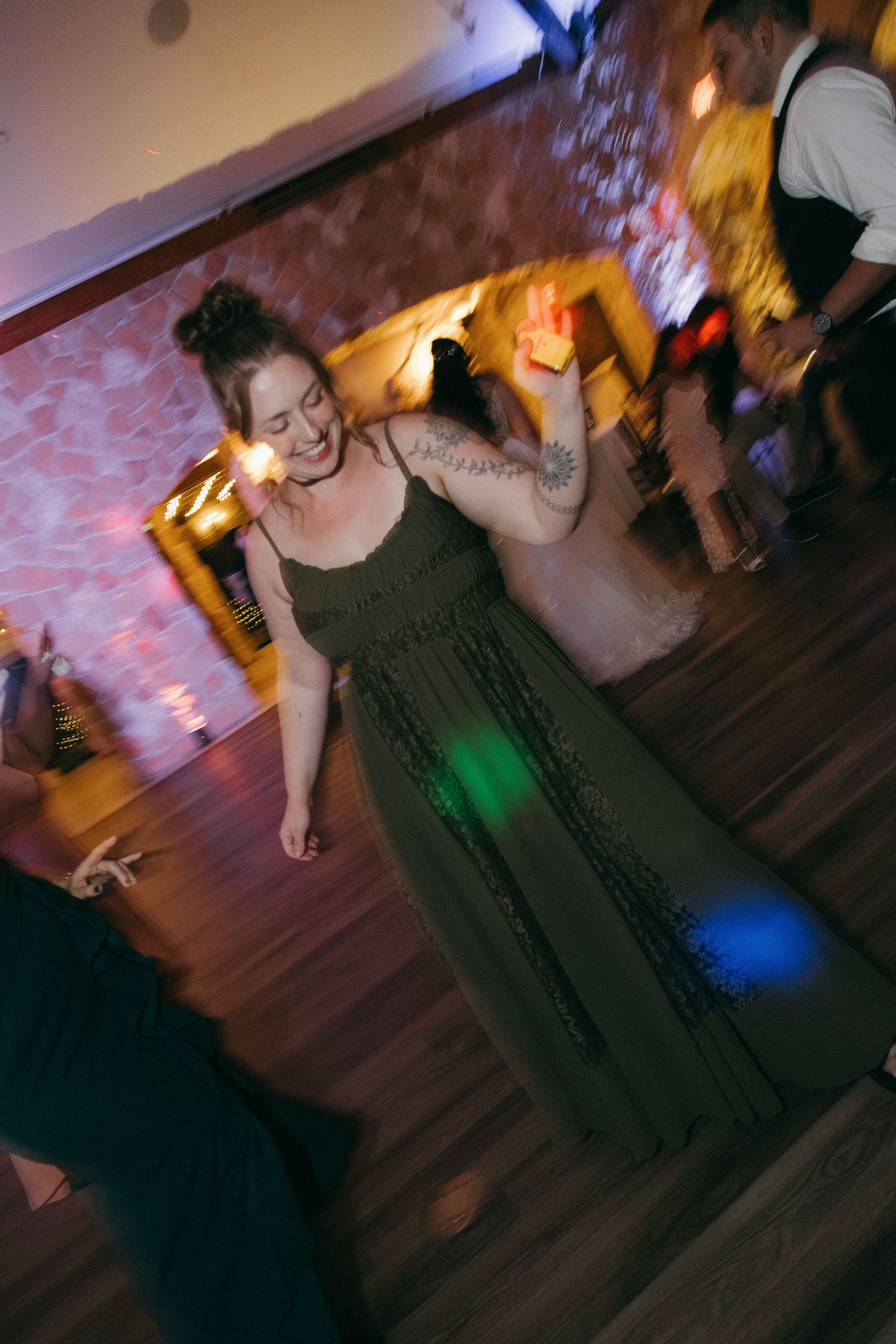 Woman in olive green dress dancing joyfully at wedding reception on dance floor.
