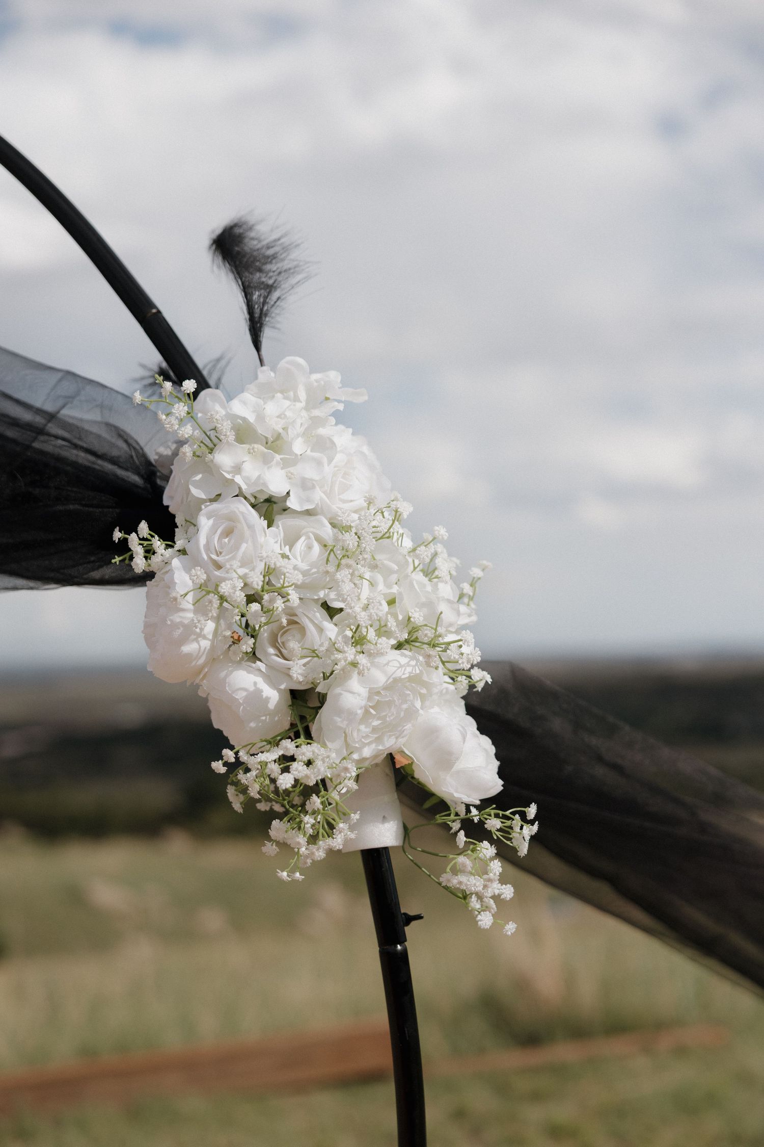 White roses and baby's breath bouquet tied with black tulle on an outdoor wedding arch.