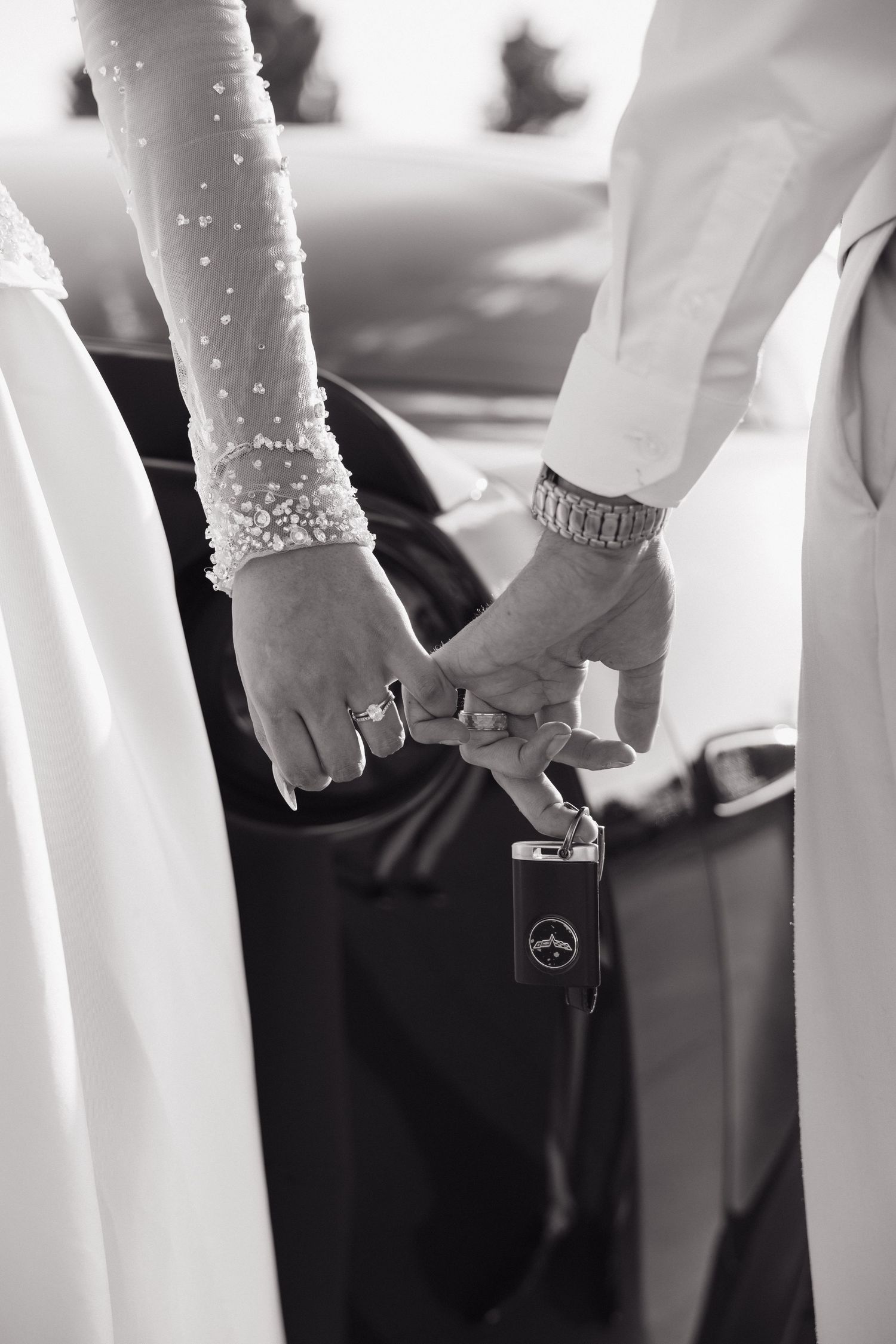 Black and white close-up of bride and groom holding hands with luxury car key.