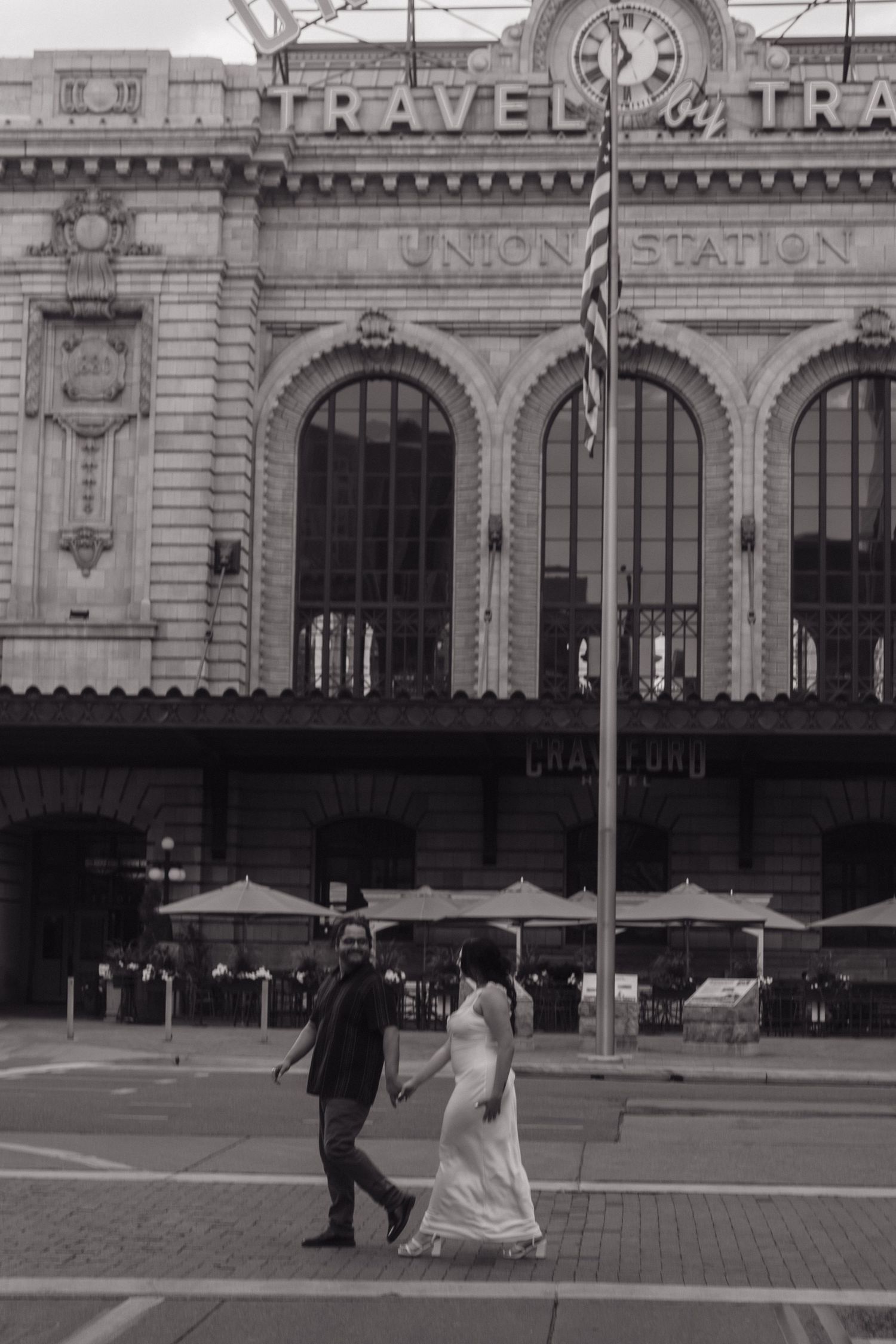 A couple poses in front of a historic train station with classic architectural details.