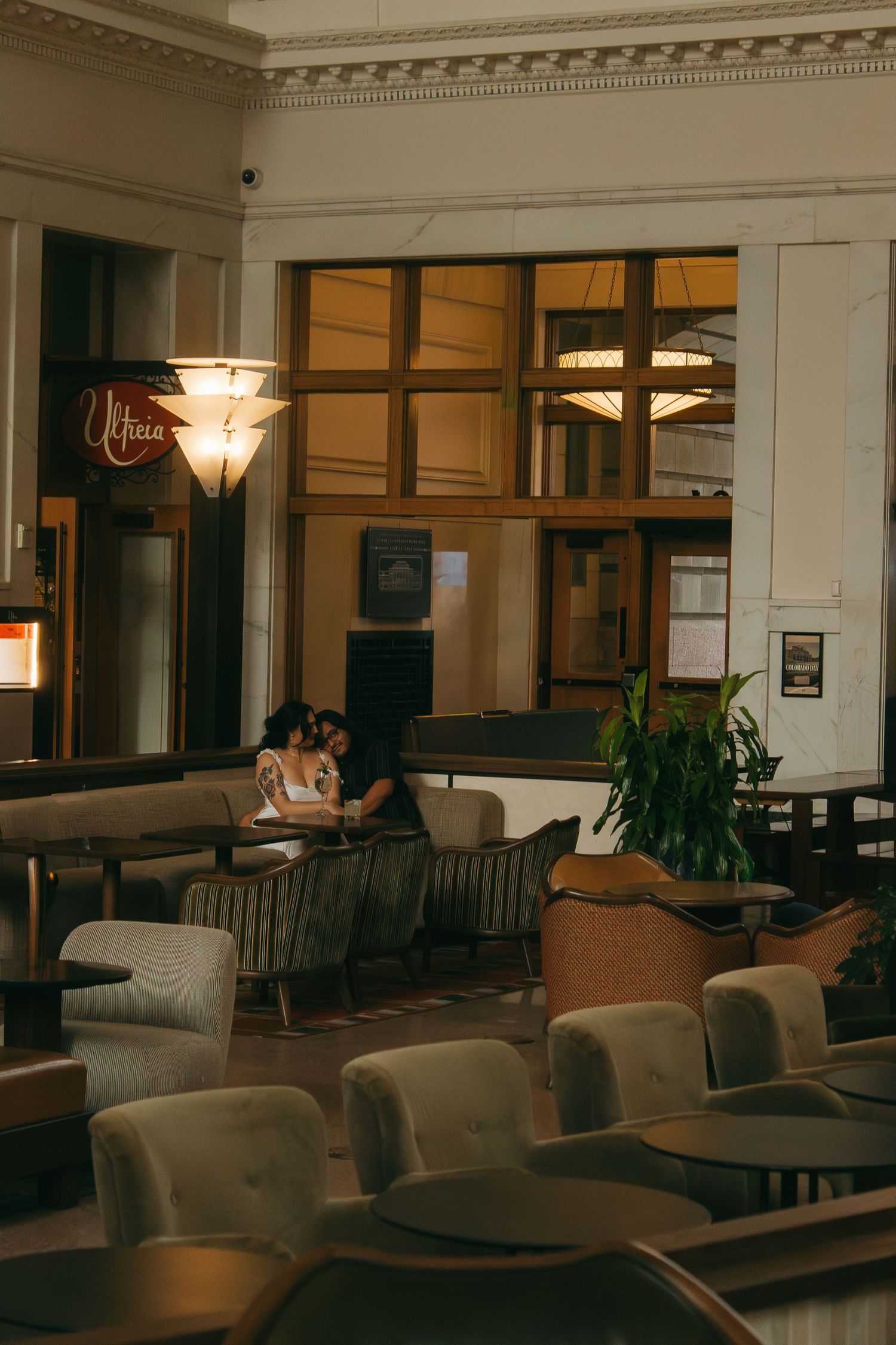 Dimly lit hotel lobby lounge area with gray couches and classic architectural details illuminated by warm lighting.
