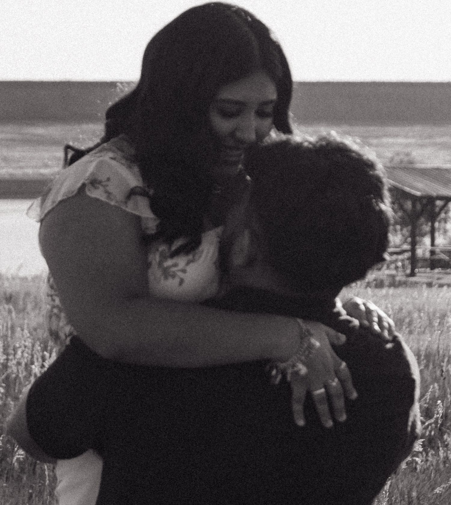 A black and white photo capturing a tender embrace in a grassy field.