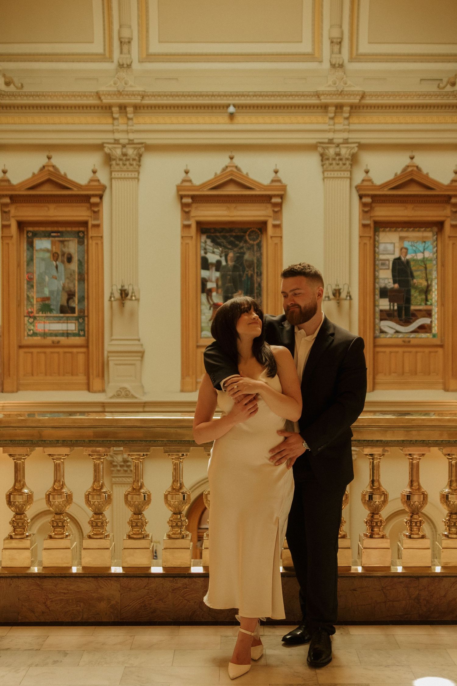 Elegant couple posing in formal attire against ornate classical architecture and decorative balustrades.
