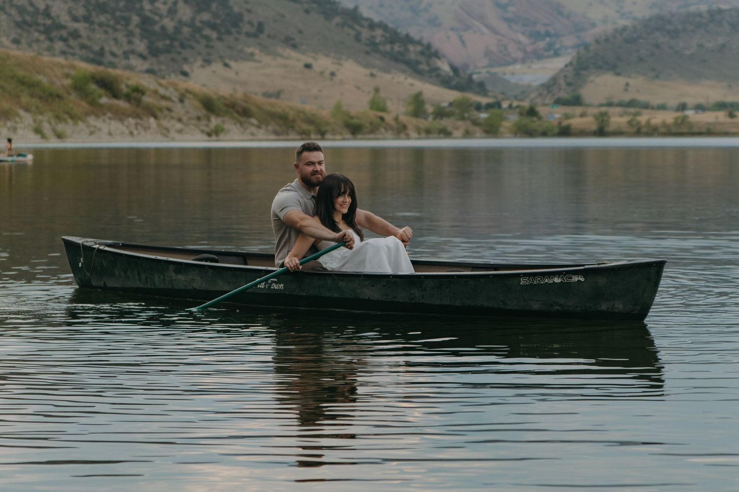 Wide landscape shot of canoe on serene lake with mountains and trees in background.