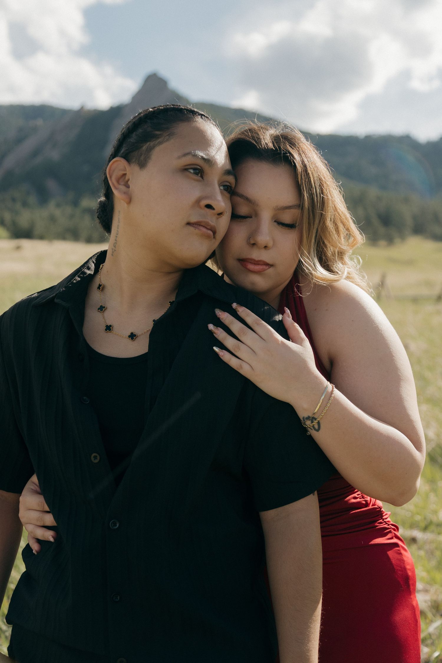 Couple embracing in a field with the Flatirons mountains in Boulder, Colorado behind them.