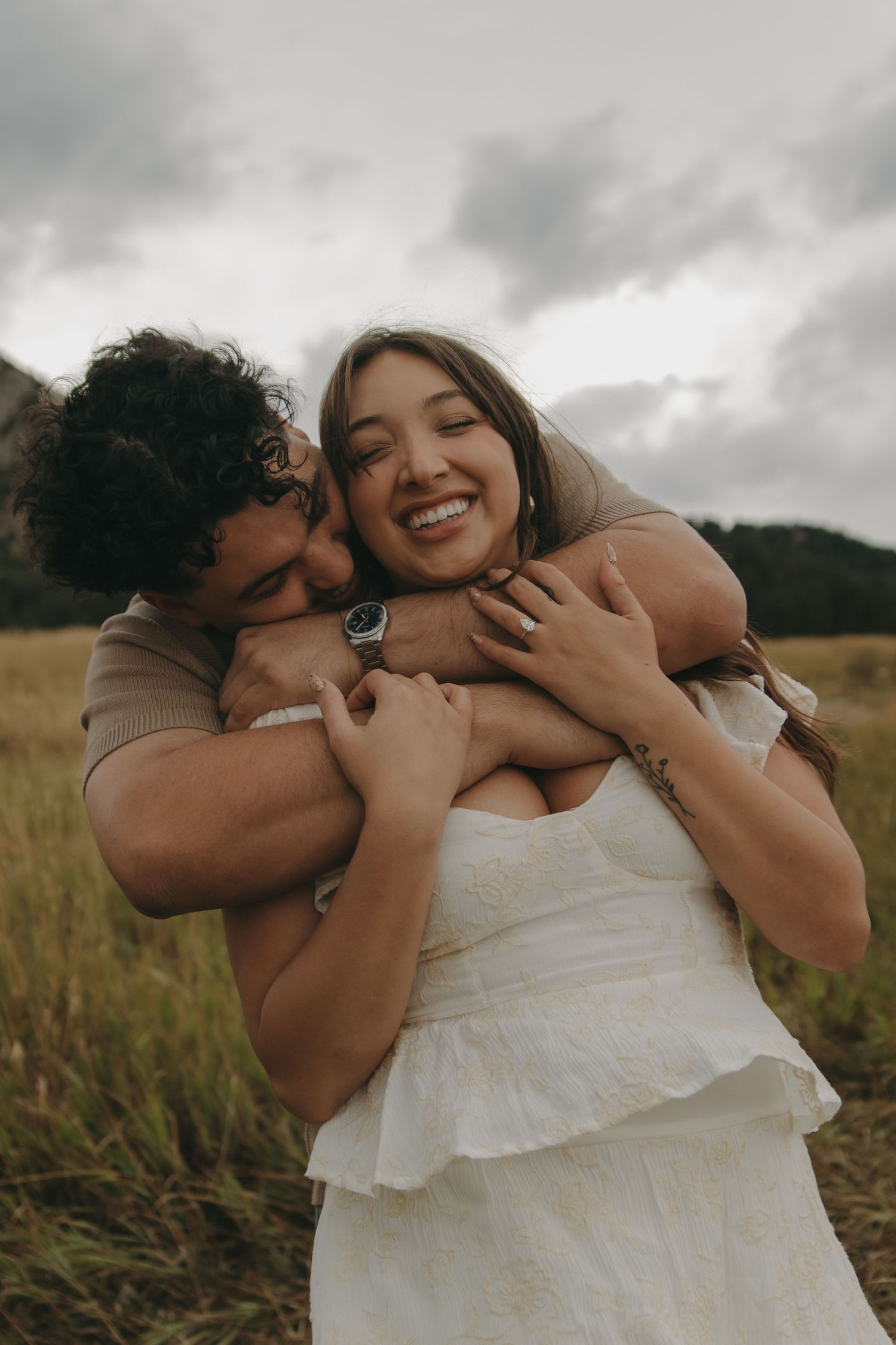 Man hugging woman from behind as she laughs joyfully in a mountain meadow.