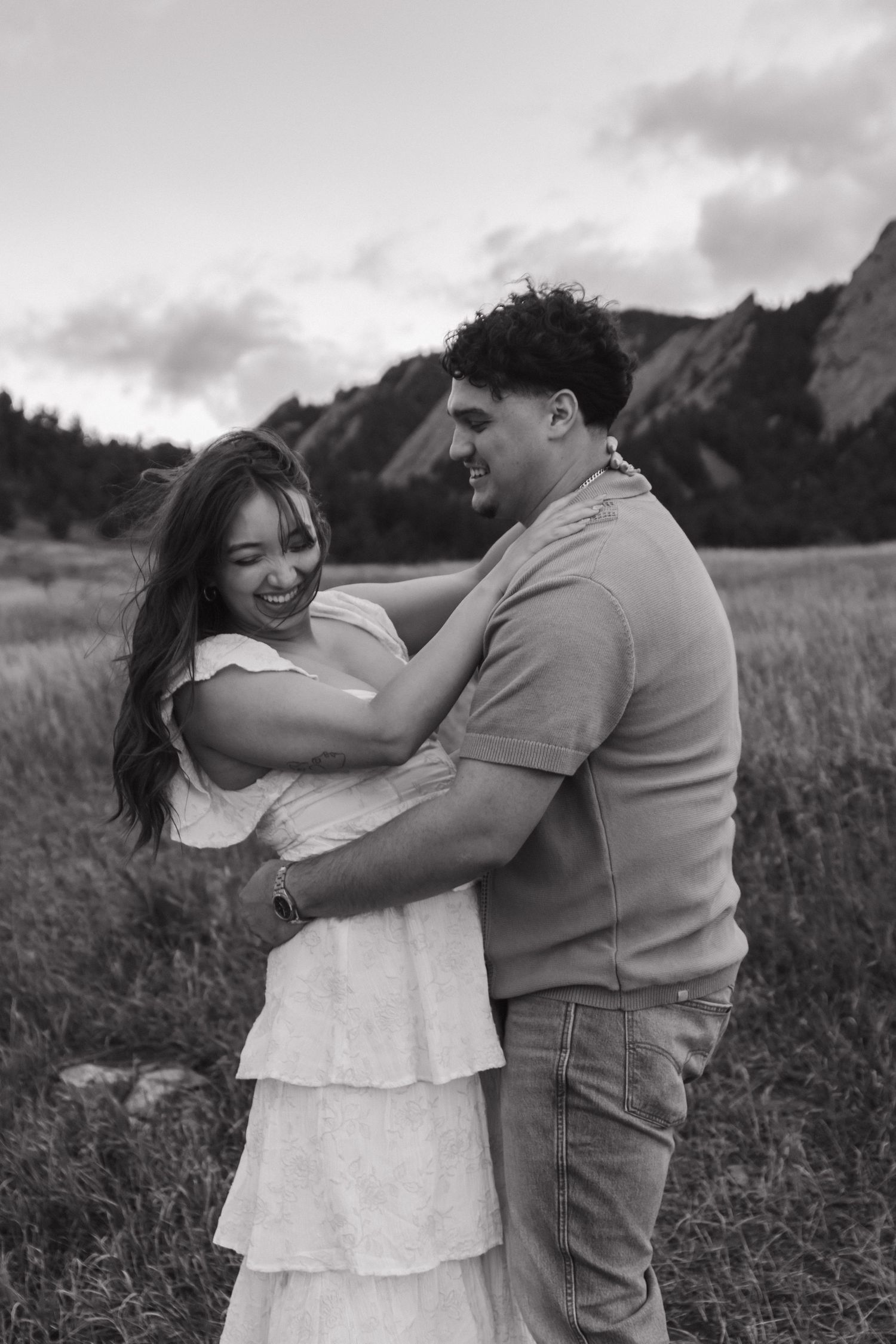 Black and white photo of a couple embracing and laughing together in a mountain meadow.