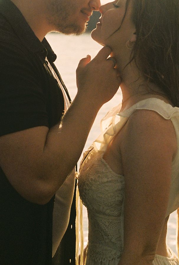Intimate close-up of couple about to kiss in warm golden backlight near a lake.