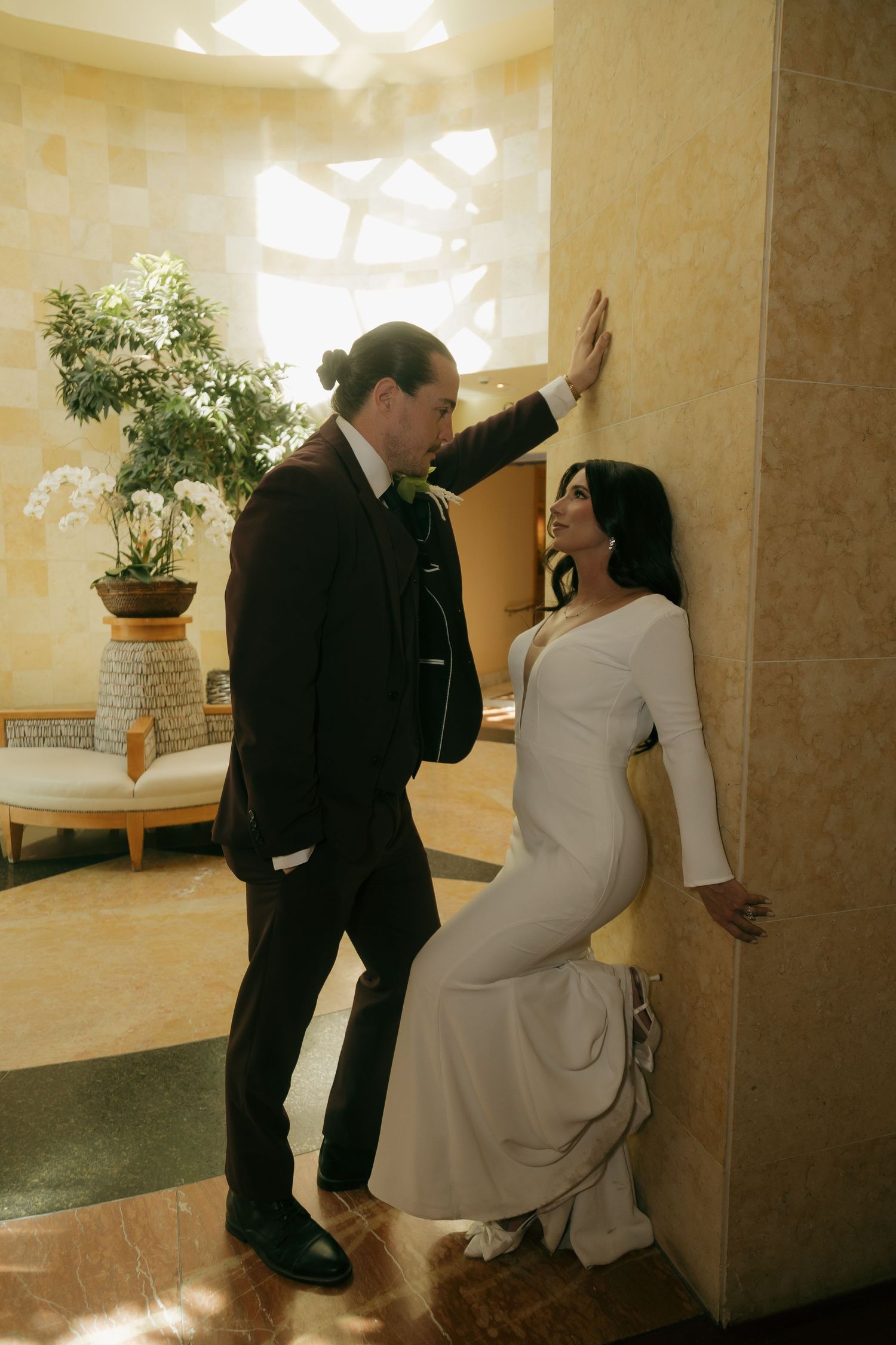 Elegant bride in white gown and groom in dark suit pose in a luxurious marble venue.