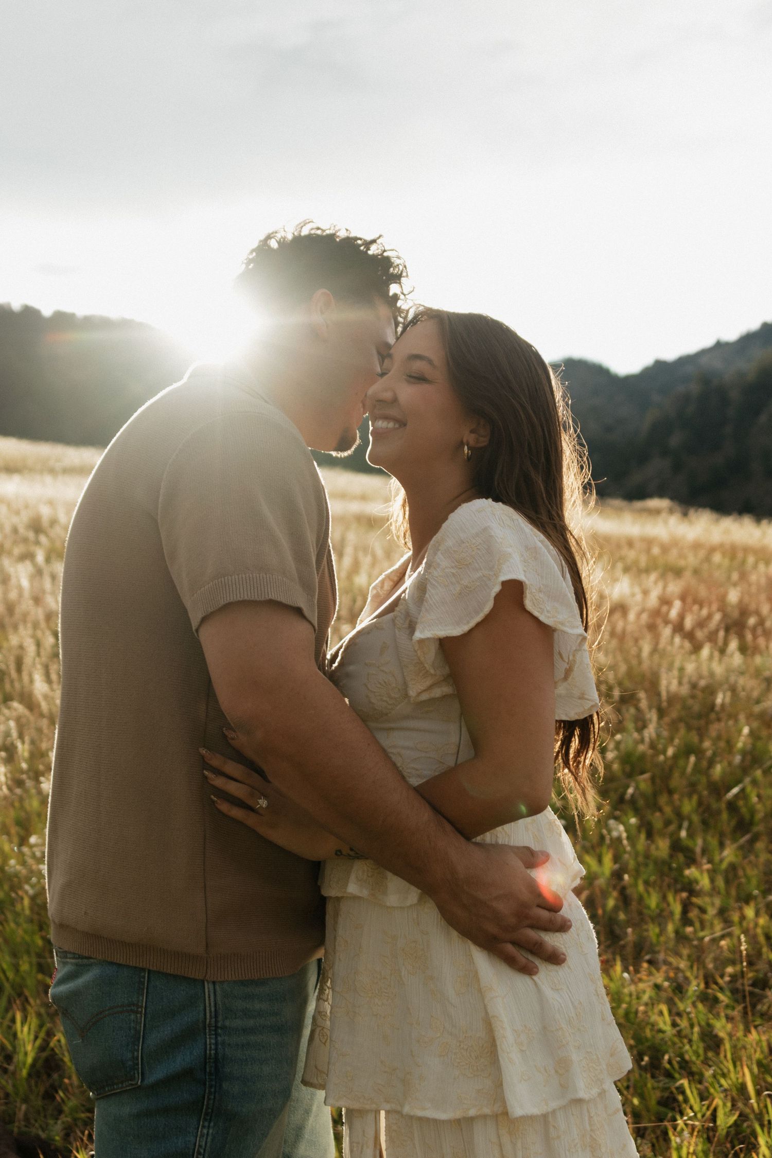 A romantic moment captured in a sunlit meadow as a couple shares an intimate embrace.