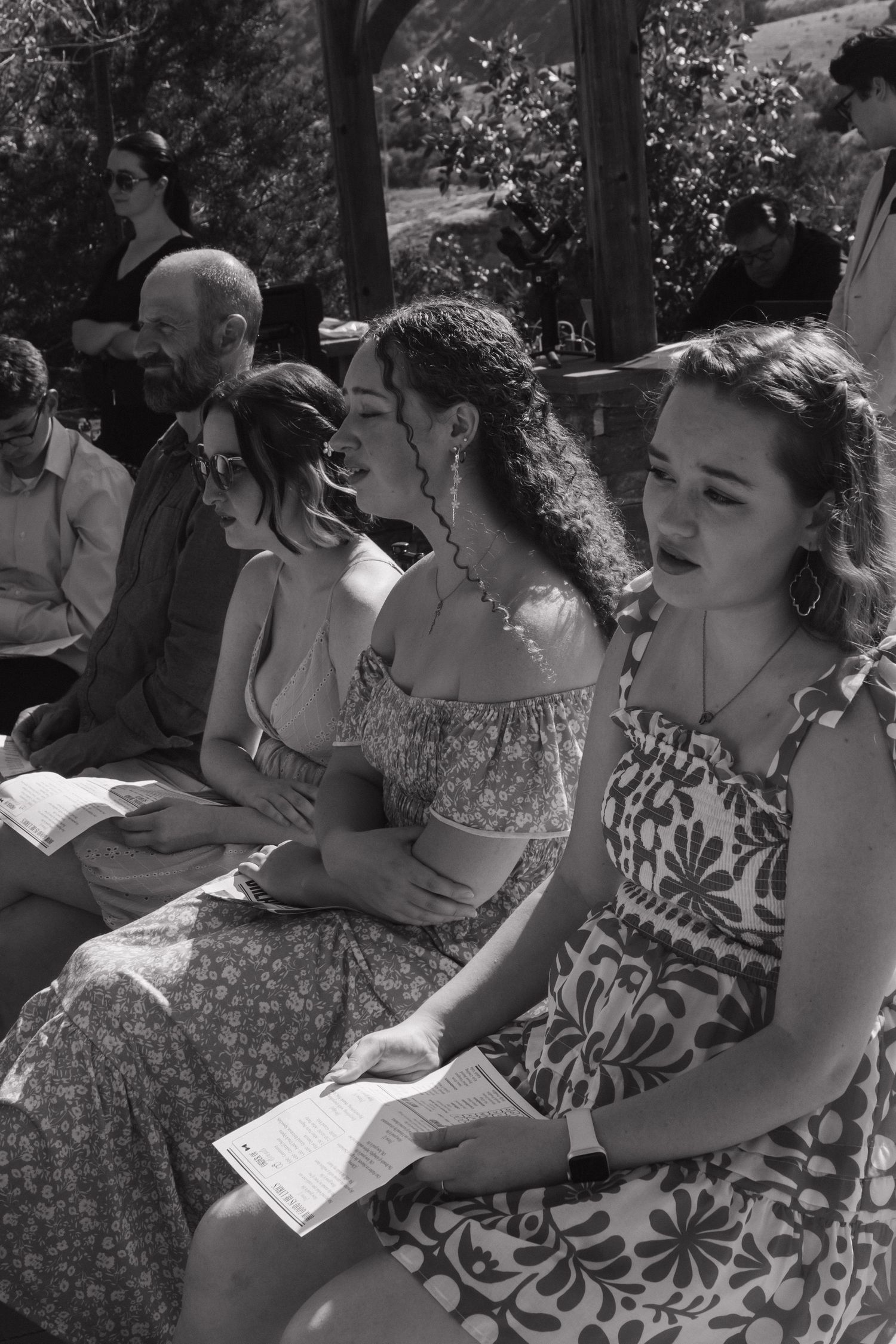 Wedding guests in vintage-style floral dresses seated outdoors during ceremony.