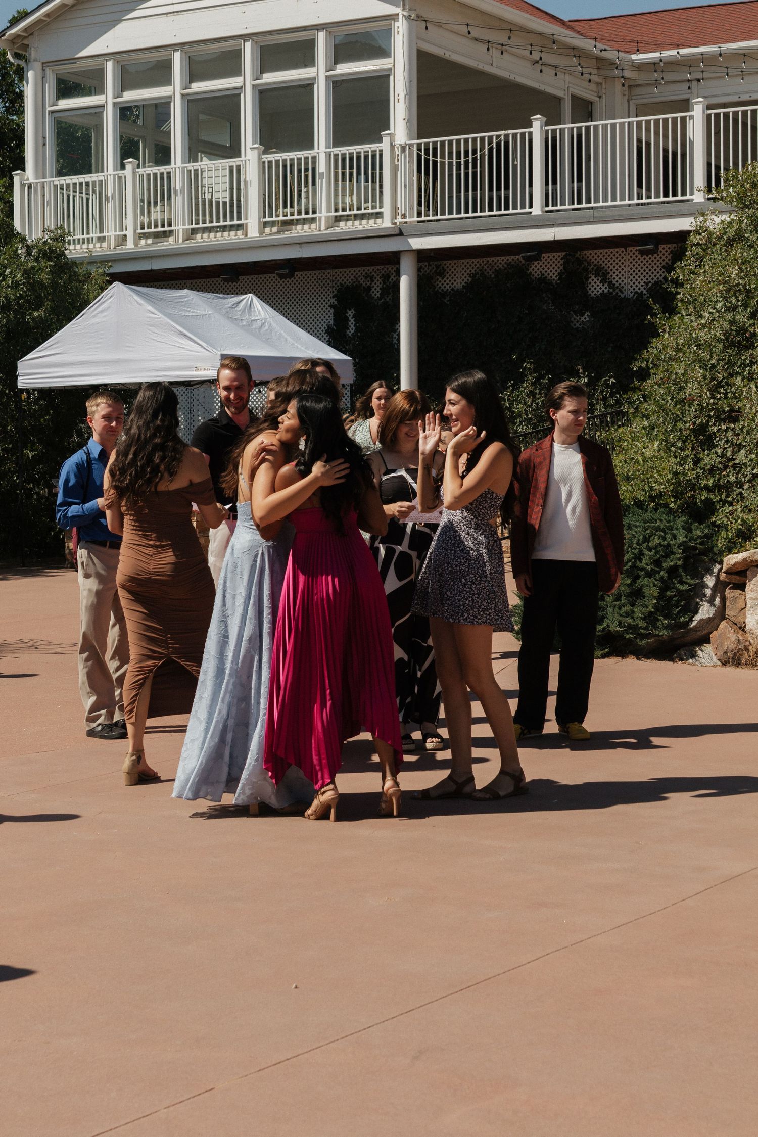 Wedding guests gathered outside venue under white tent on sunny day.