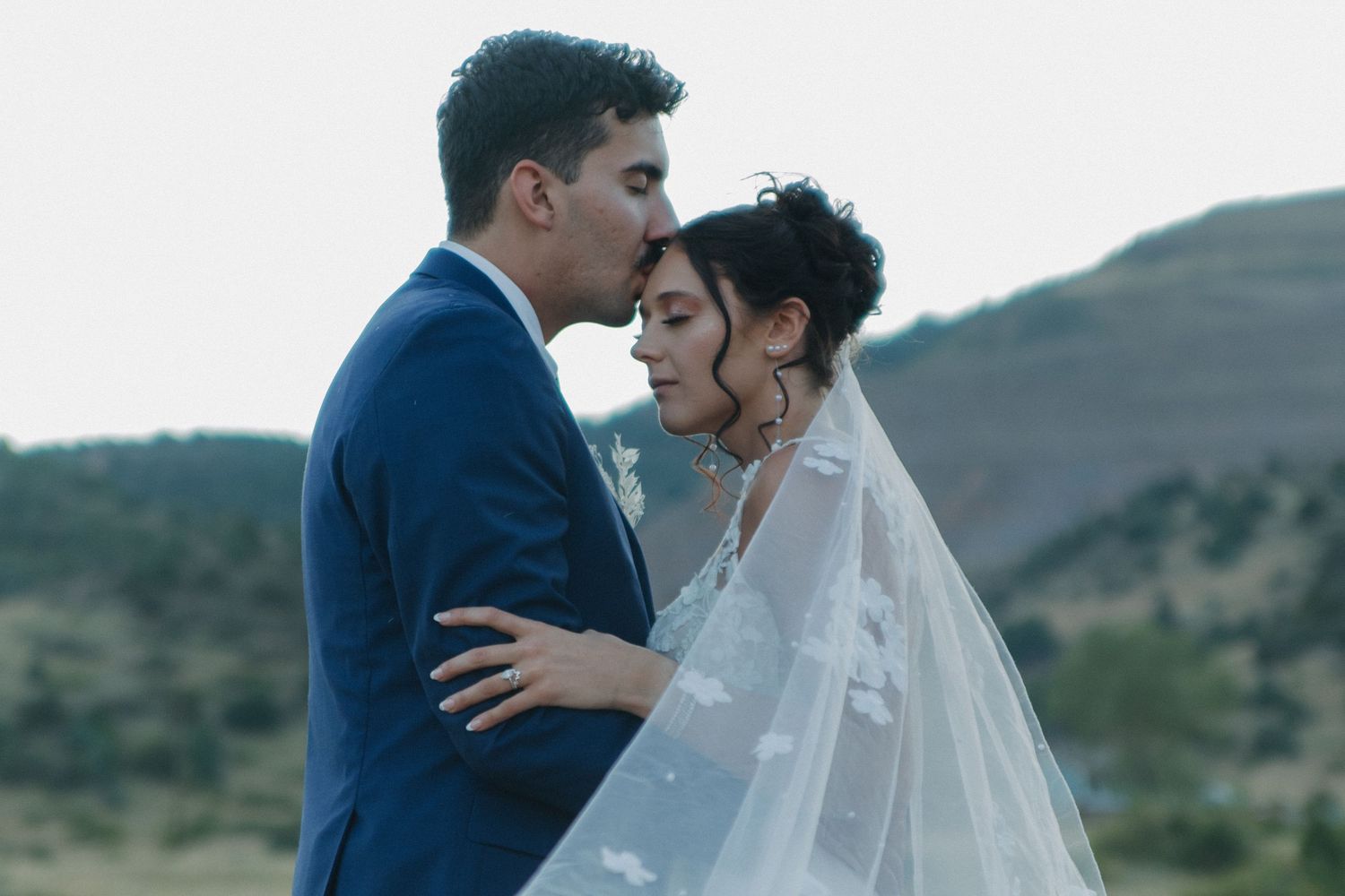 Couple sharing intimate moment during outdoor wedding with mountains in background.