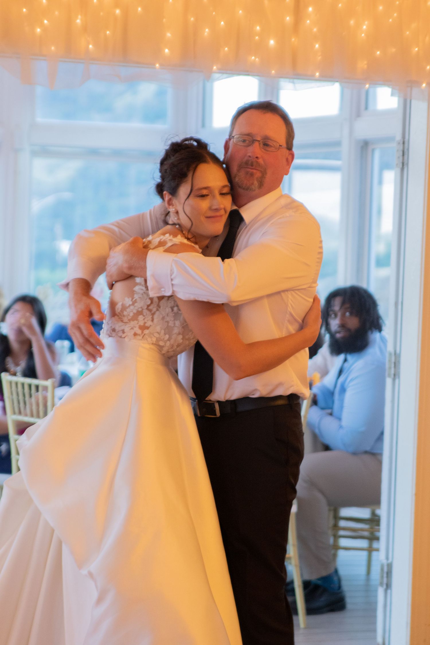 Warm-lit indoor wedding dance with string lights creating romantic ambiance.