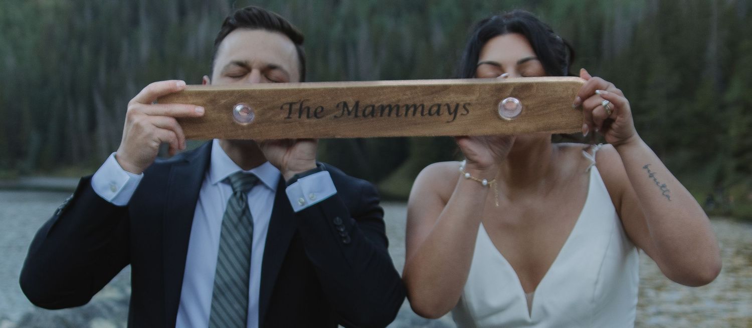 Couple holding rustic wooden wedding sign in mountain setting.