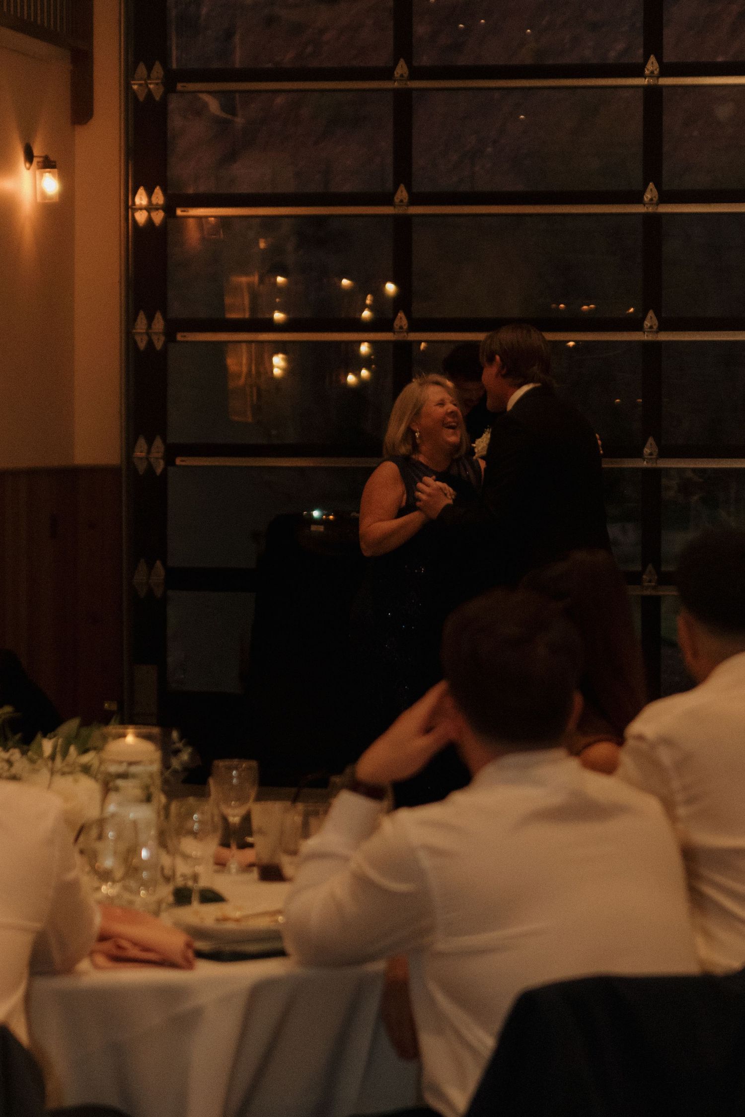 Diners seated at elegant white-clothed tables in a dimly lit restaurant with warm ambient lighting.