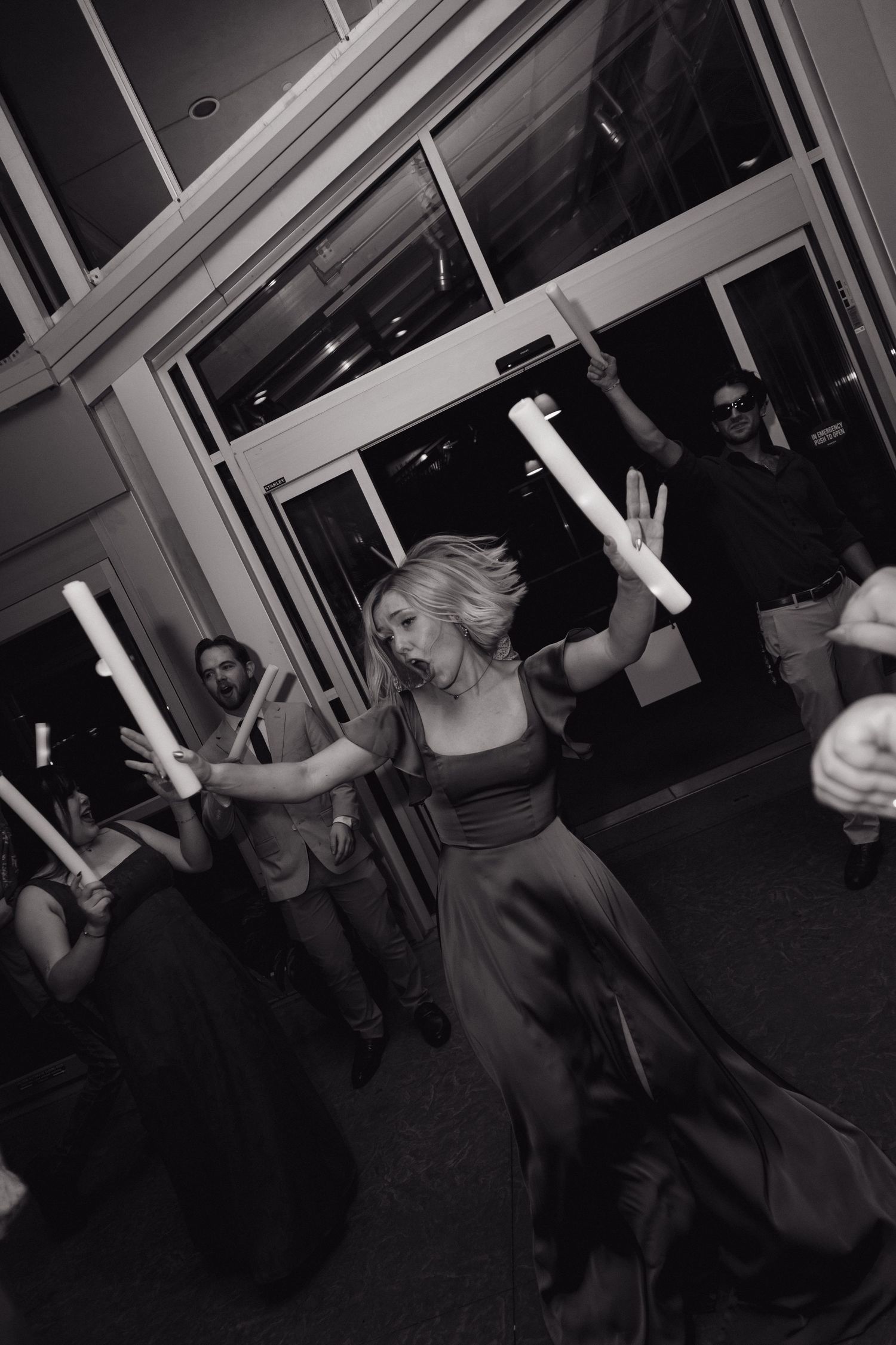 Black and white photo of a woman dancing with glow sticks at a nighttime outdoor celebration.