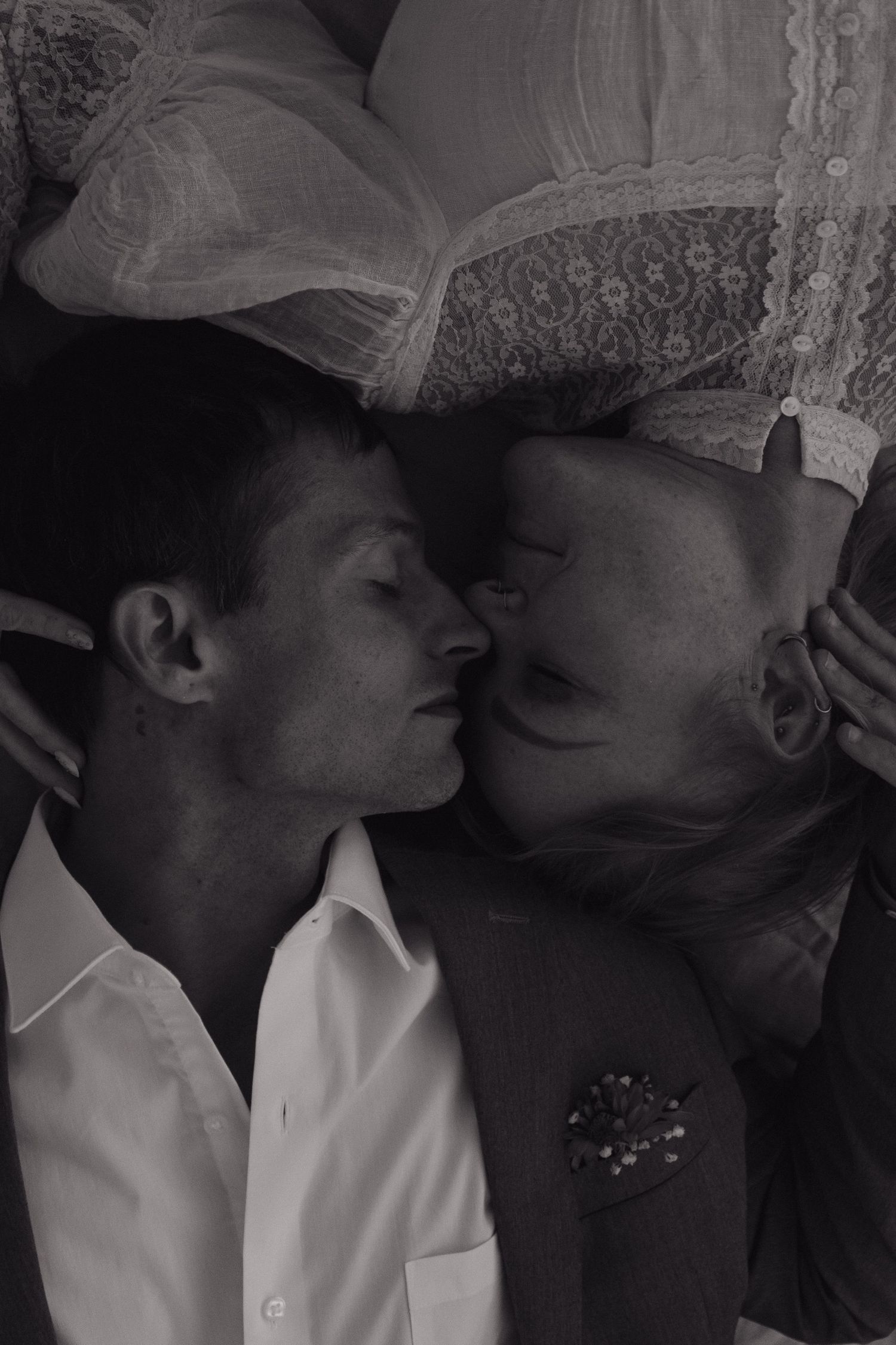 Black and white photo of a bride and groom sharing a tender kiss while lying down together.