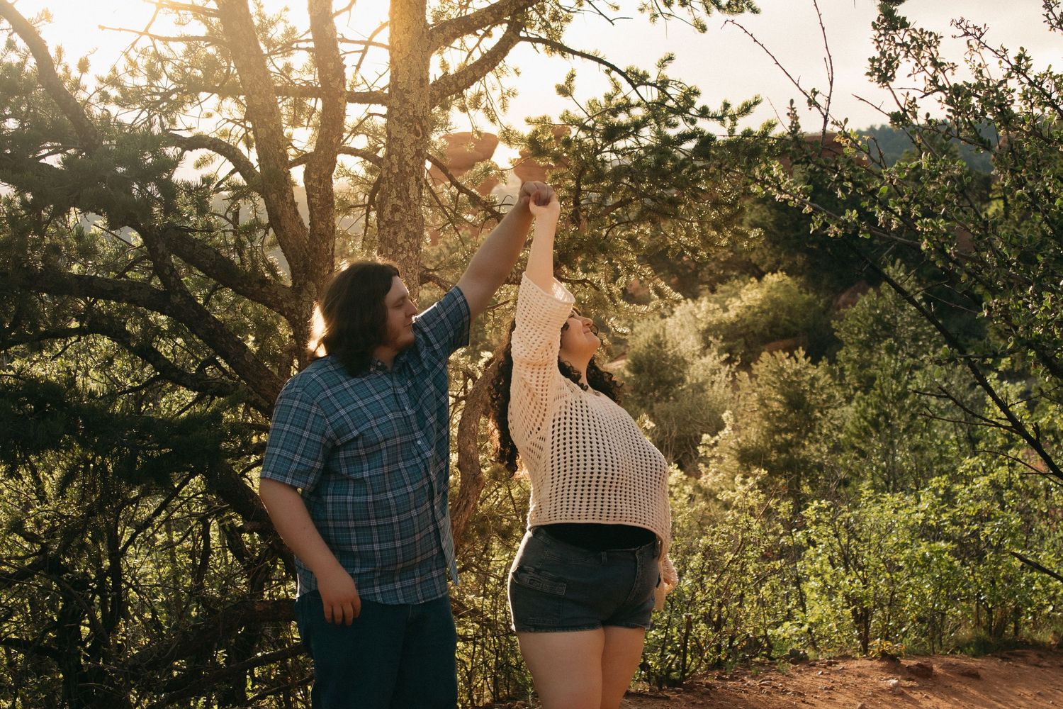 A couple dances playfully on a rocky trail during golden hour.