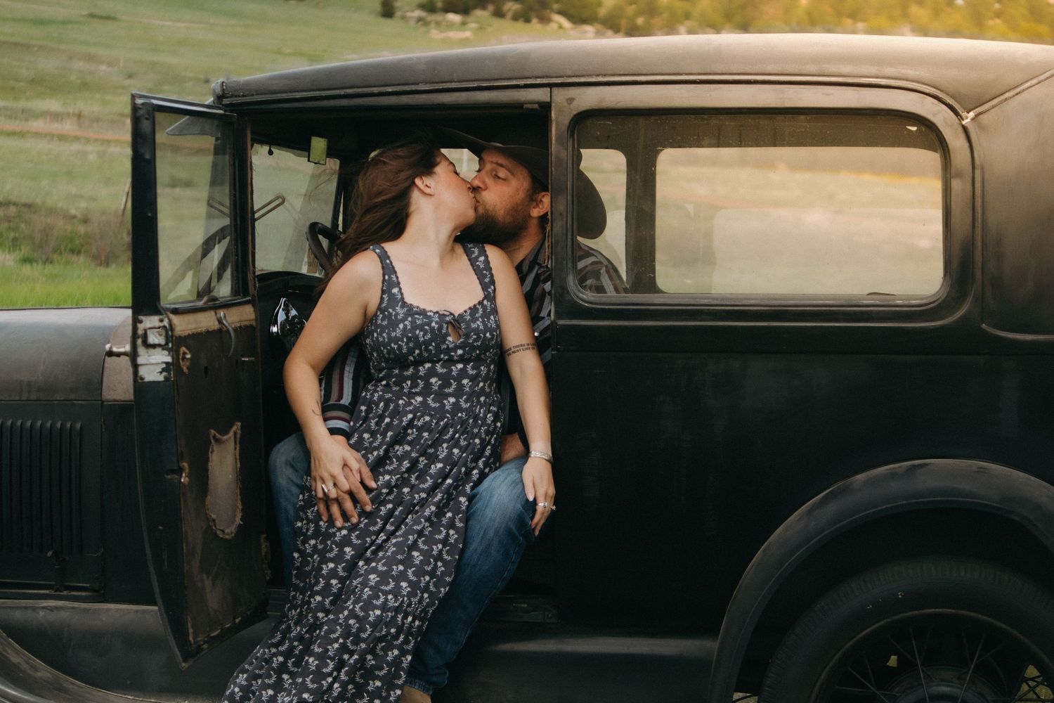 Couple sharing intimate moment in antique black car during golden hour.