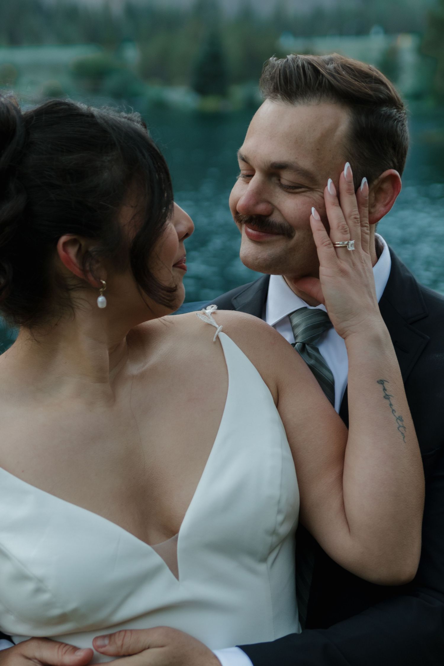 A tender moment between newlyweds against a mountain lake backdrop at sunset.