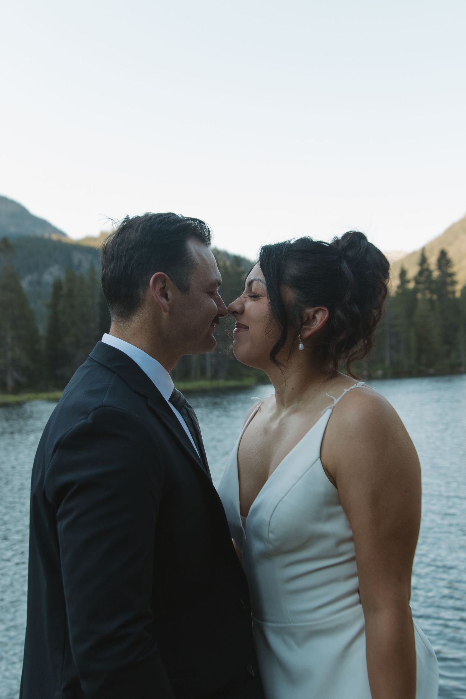 Romantic lakeside wedding photos with mountains and pine trees creating a stunning backdrop.