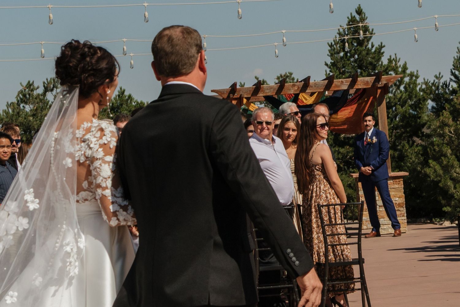 Outdoor wedding ceremony with string lights and guests gathering.