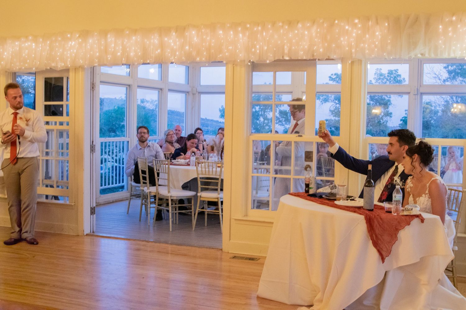 Interior view of an elegant white wedding reception venue with large windows and bright natural lighting.