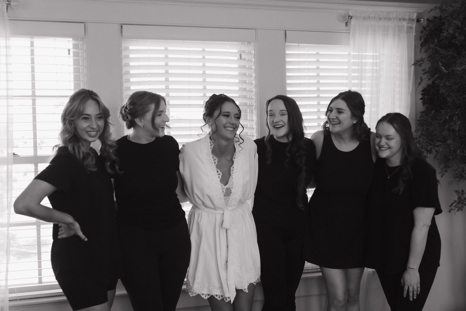 Wedding party members dressed in black pose together in a stylish indoor setting.